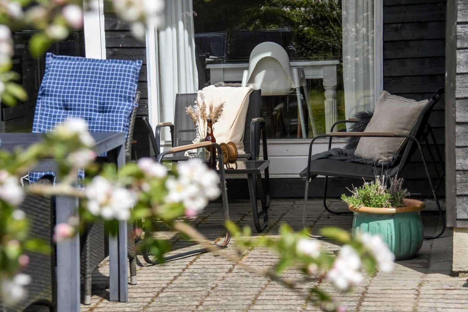 Terrasse mit Sitzgelegenheiten und Pflanzen vor einem Haus mit dunklem Holzverkleidung.