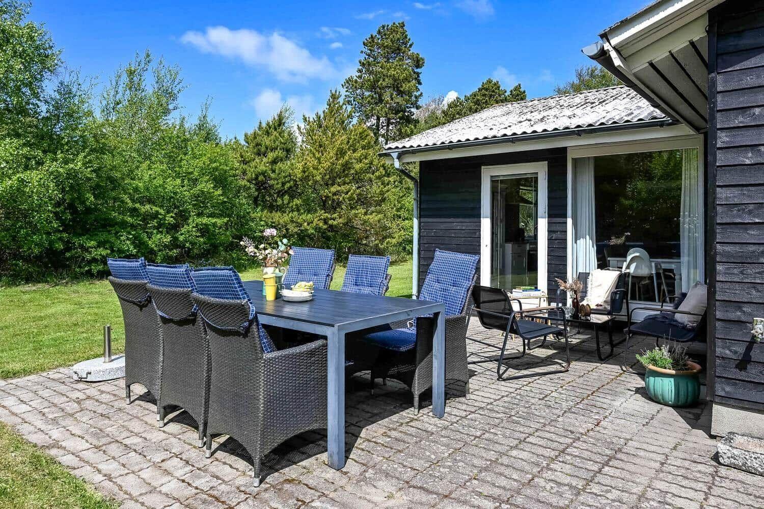 Terrasse mit Esstisch und Stühlen vor einem Haus mit Balkon.