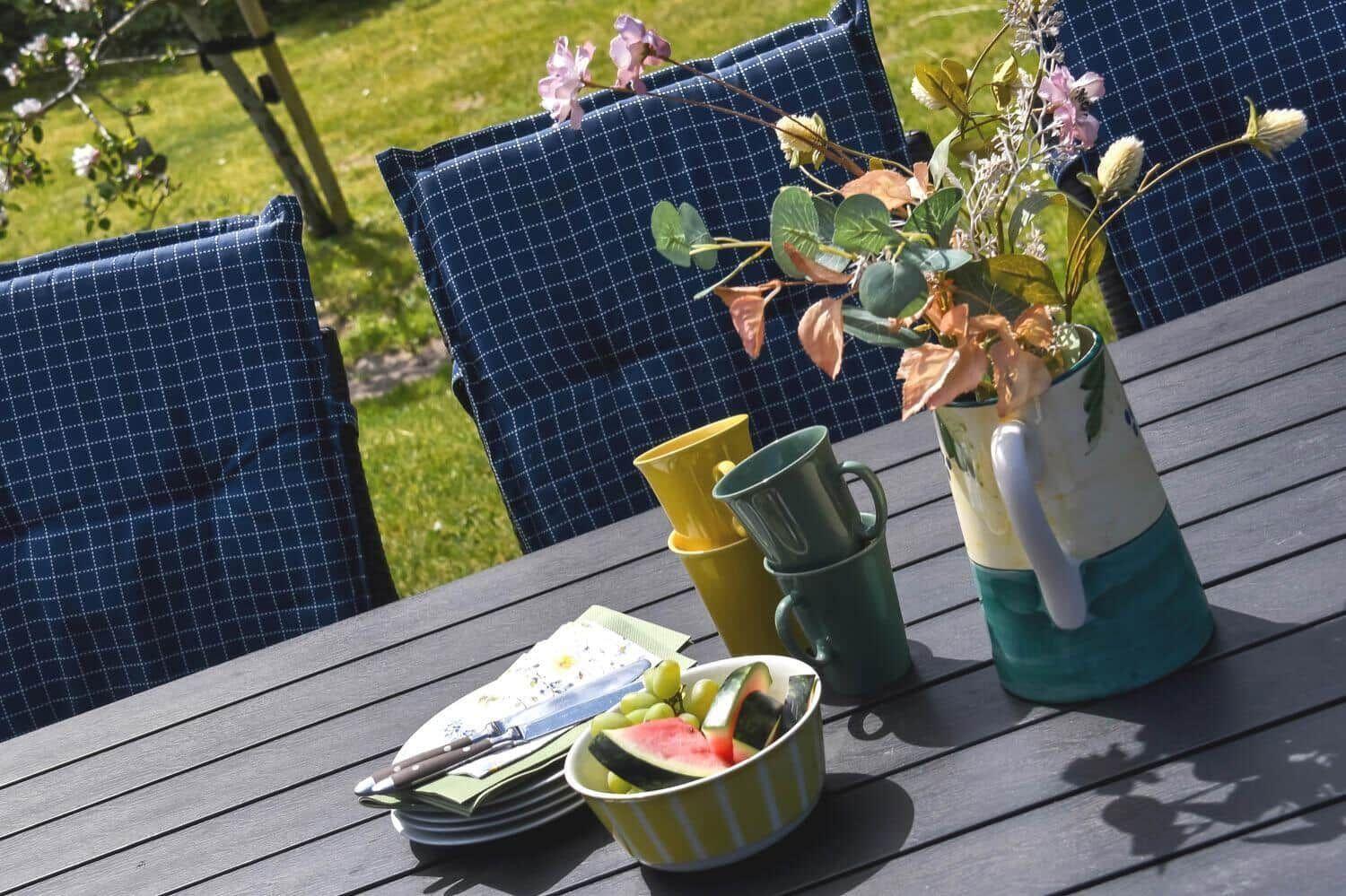 Außenbereich mit Tisch, Stühlen und Obst. Blumen in Vasen und Tassen.