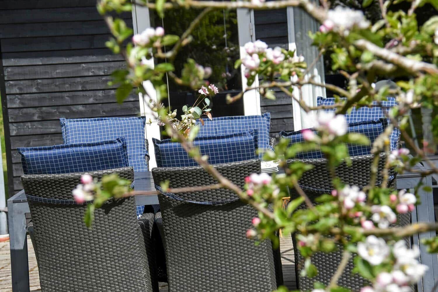 Außenbereich mit Gartenstühlen und Kissen vor einem Haus mit dunklem Holzverkleidung.