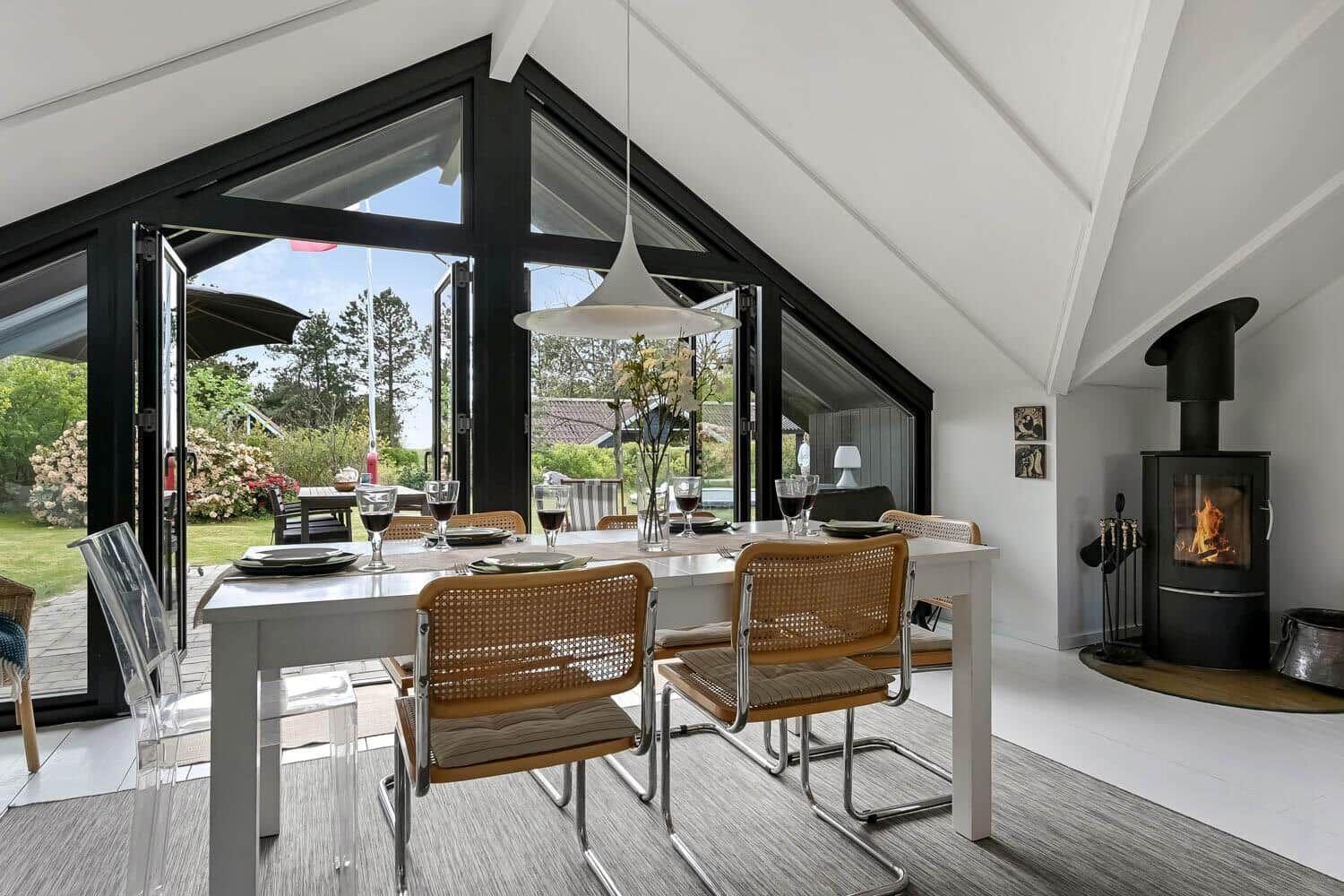 Esszimmer mit Tisch, Stühlen und Kamin. Große Fensterfront zur Terrasse.