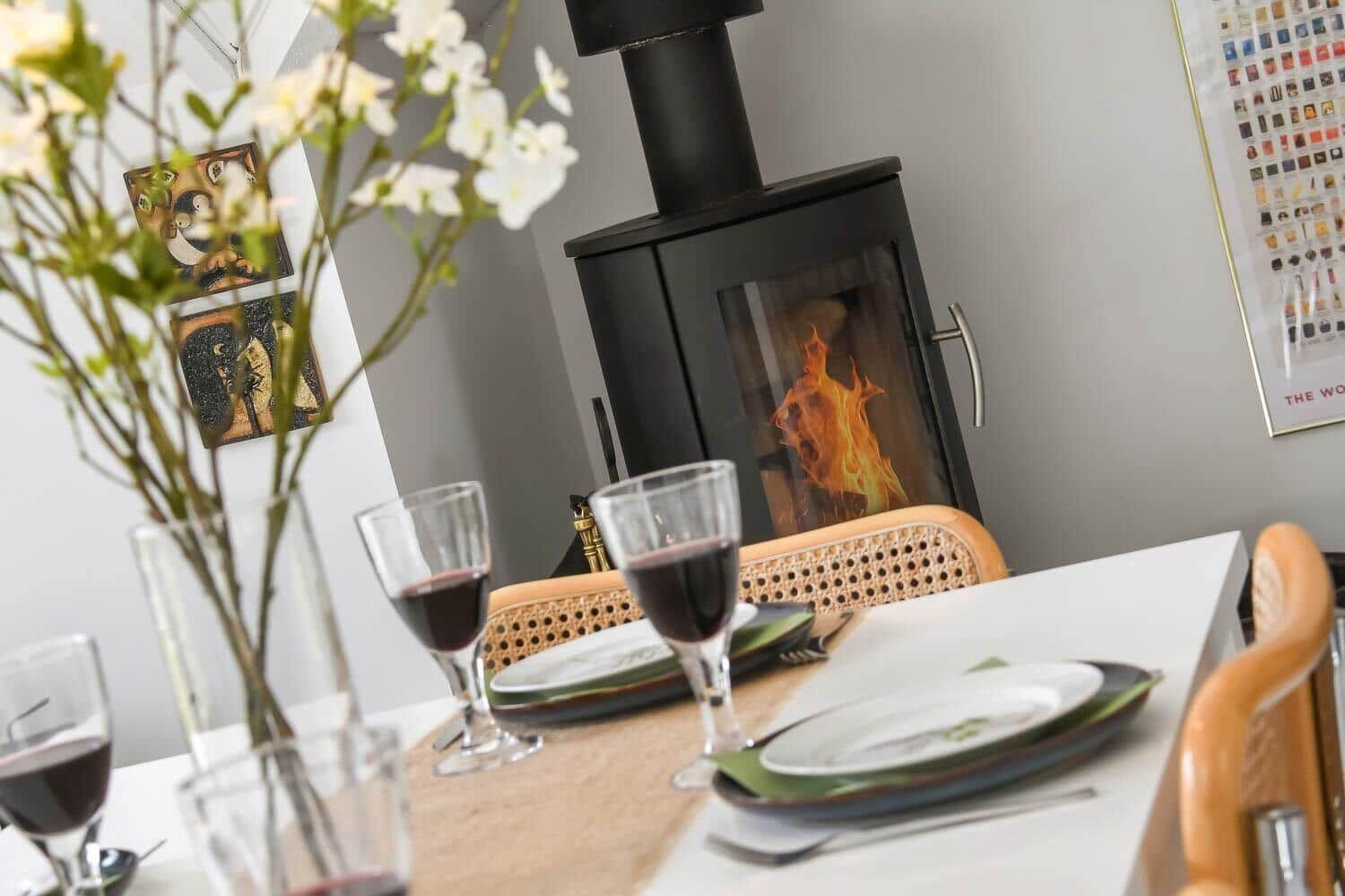 Tisch mit Gläsern und Teller vor Kamin mit brennendem Feuer.