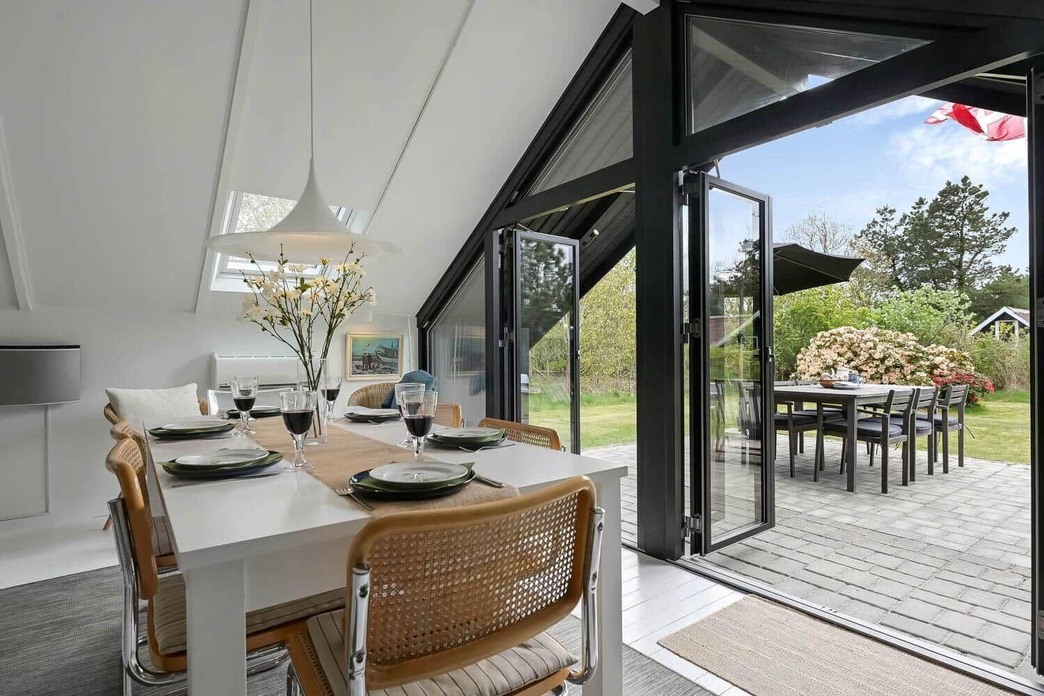 Essbereich mit Tisch und Stühlen, große Glastüren führen auf eine Terrasse mit Garten.