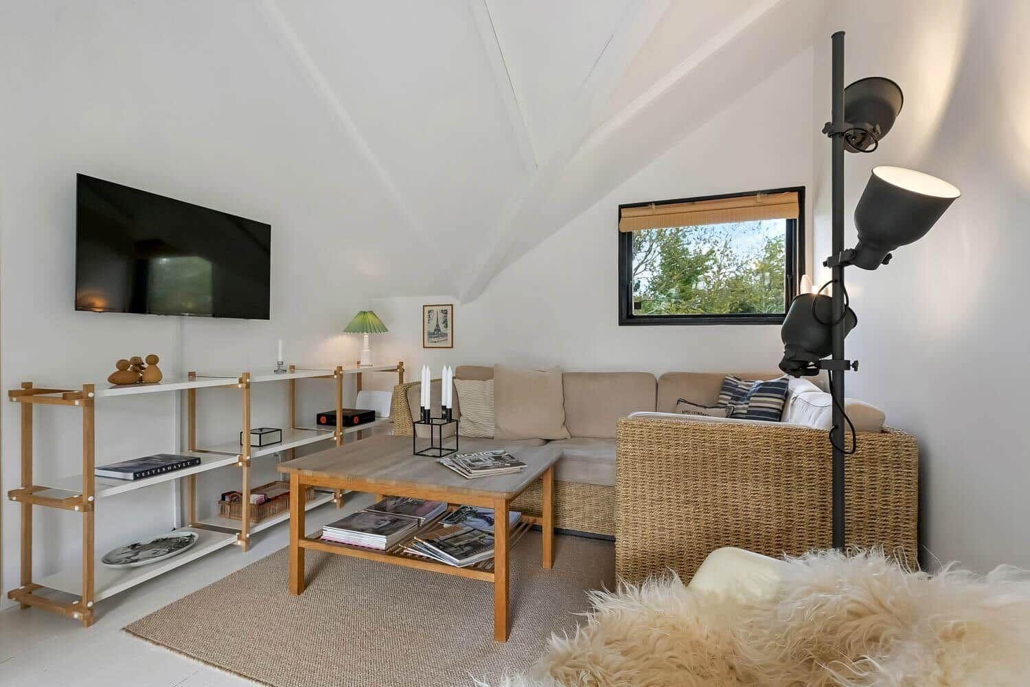 Wohnzimmer mit Sofa, Couchtisch, Fernseher und Fenster mit Blick auf Bäume.