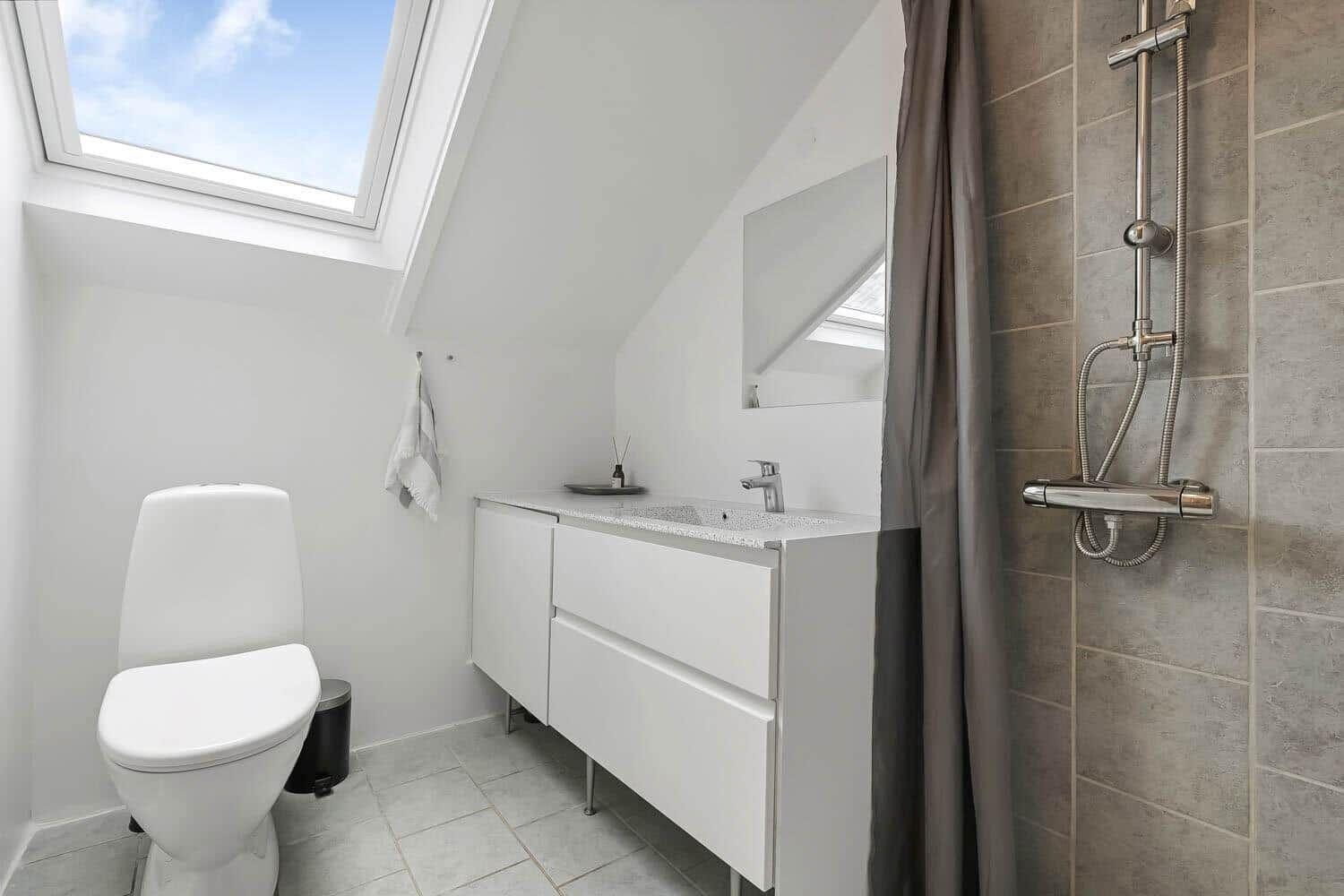 Badezimmer mit Dusche, Waschbecken und Toilette unter Dachschrägen mit Dachfenster.
