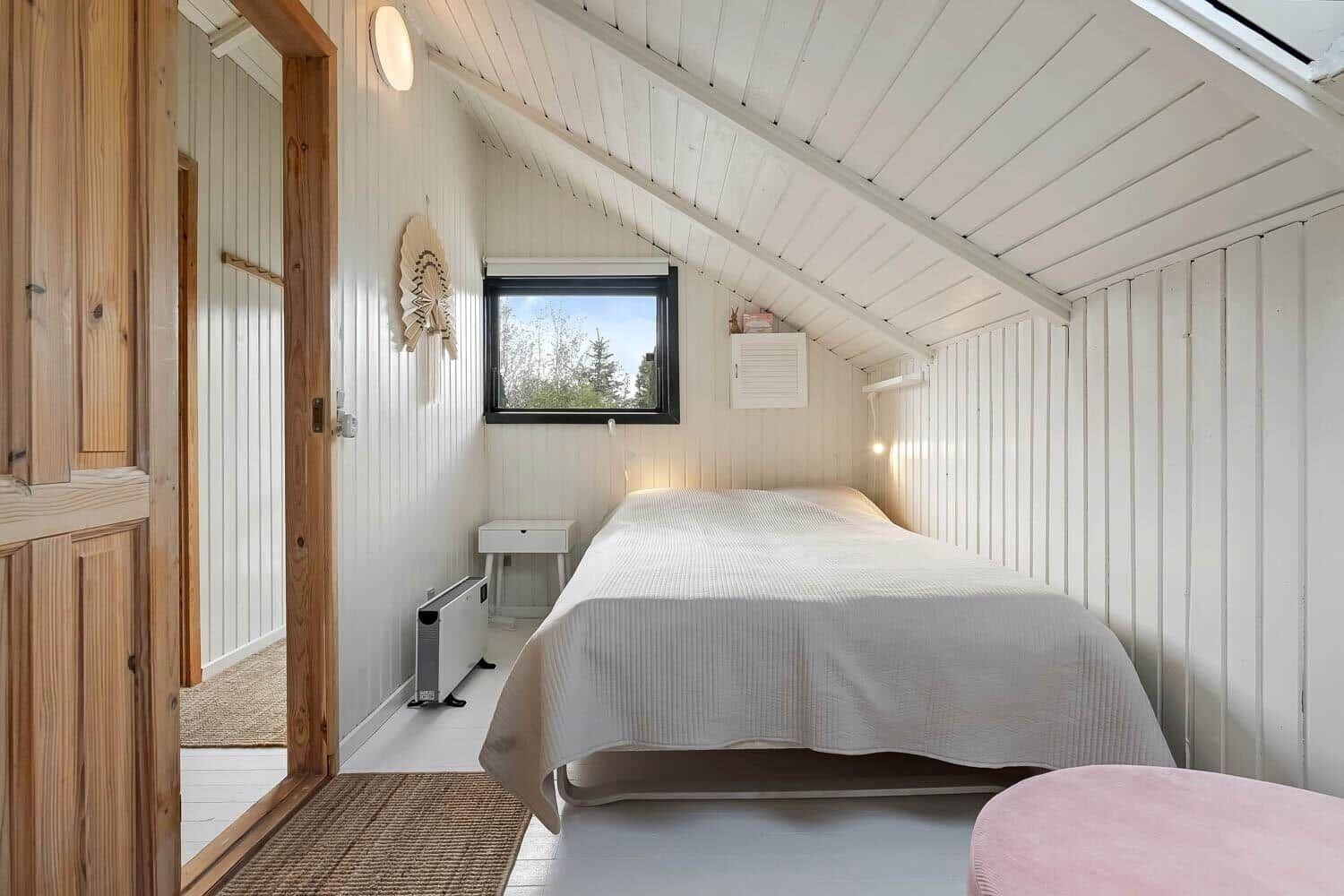 Schlafzimmer mit Bett, Fenster und Holztür. Weiße Wände und Decke.