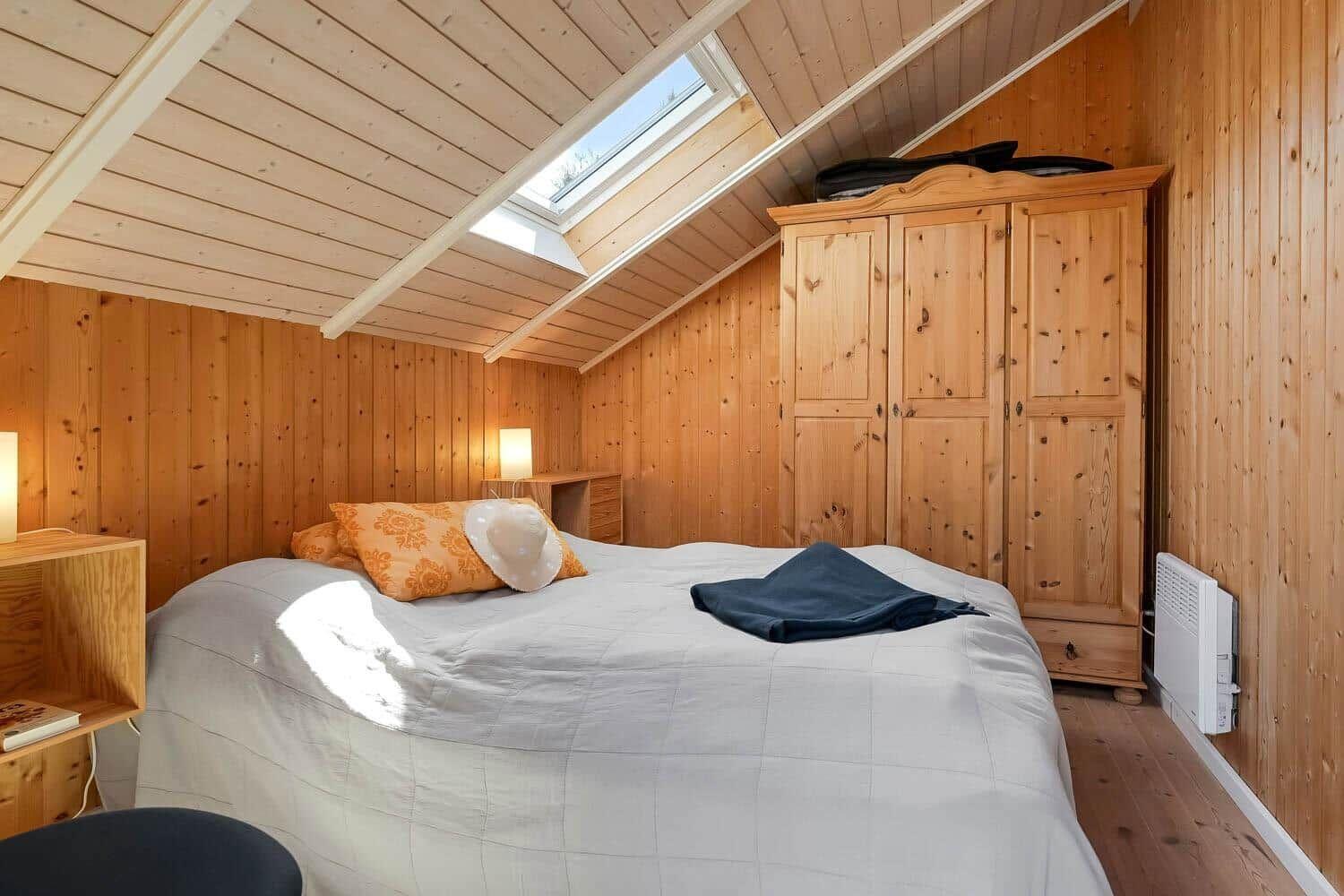 Schlafzimmer mit Holzwand, Bett, Kleiderschrank und Dachfenster.