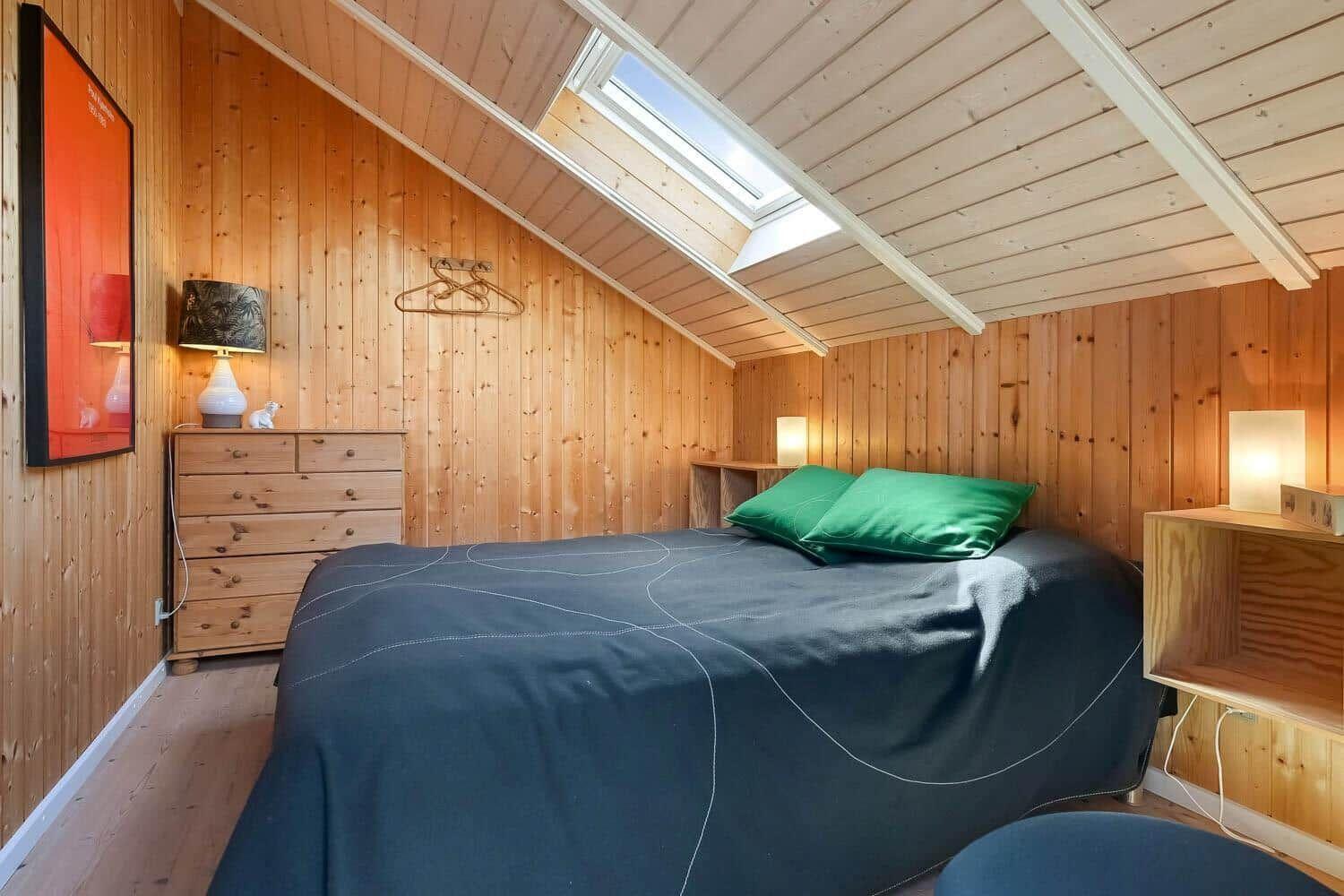 Schlafzimmer mit Holzwand, Dachschrägen, Bett mit grünen Kissen und Fenster
