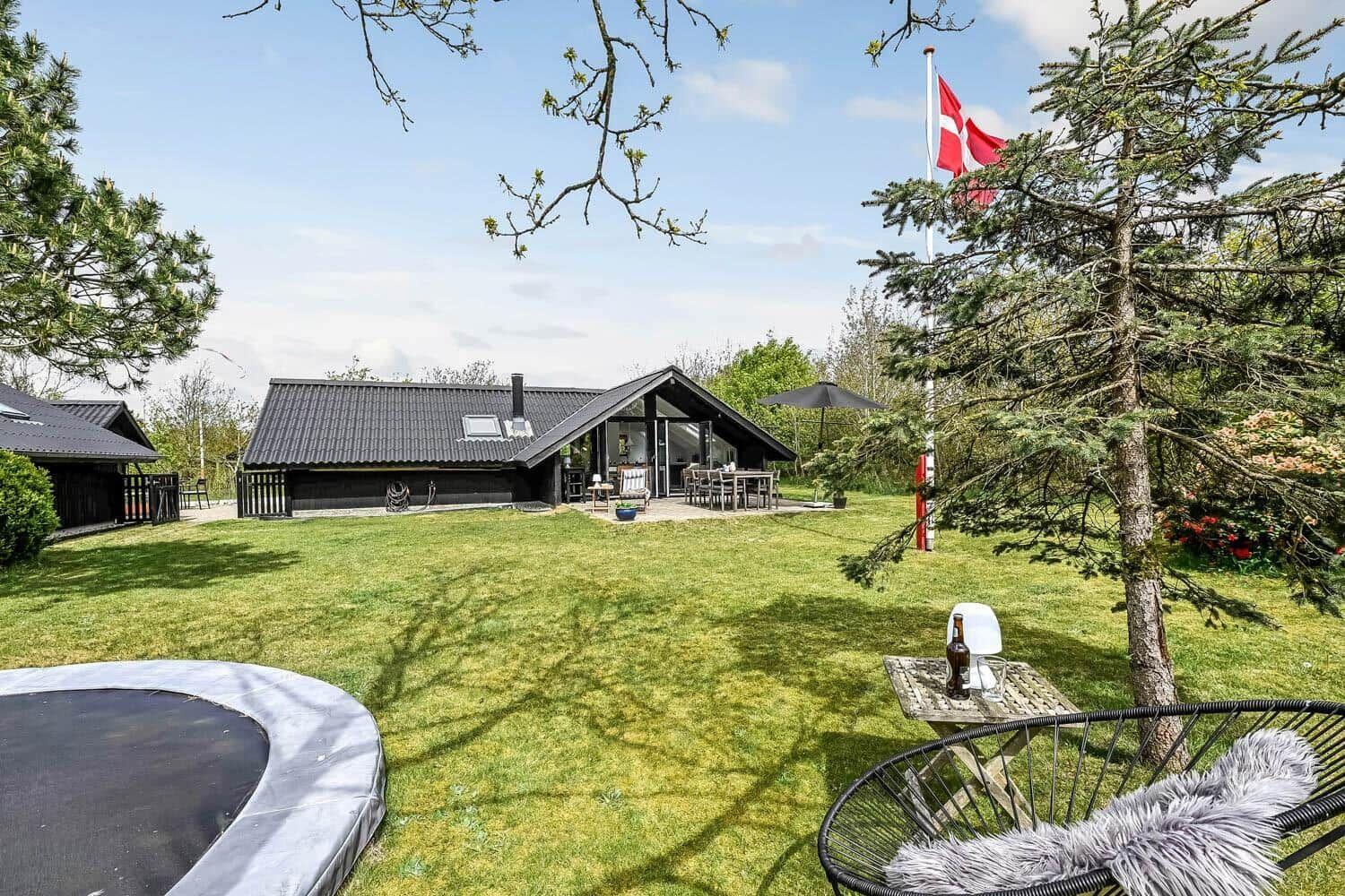 Haus mit Garten, Trampolin und dänischer Flagge. Außentisch mit Stuhl und Flasche.