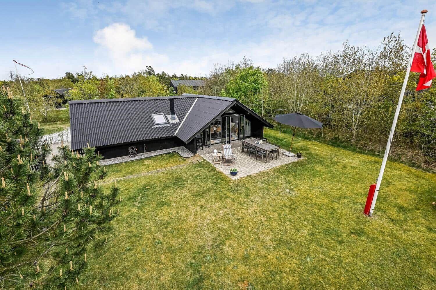 Schwarze Hütte mit Terrasse, Garten und dänischer Flagge.