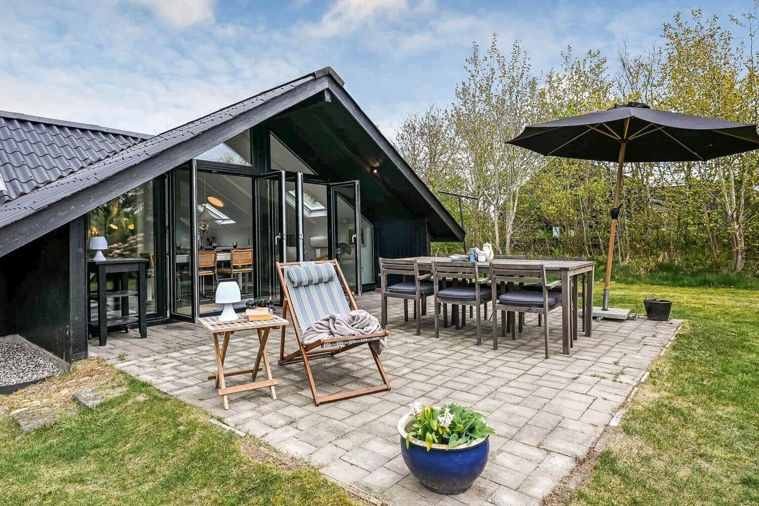 Terrasse mit Tisch, Stühlen und Sonnenschirm neben modernem Haus mit Glasfront.