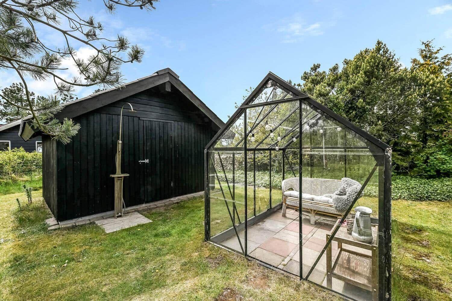 Glasveranda mit Sitzbank und Außendusche neben Holzhaus im Garten.