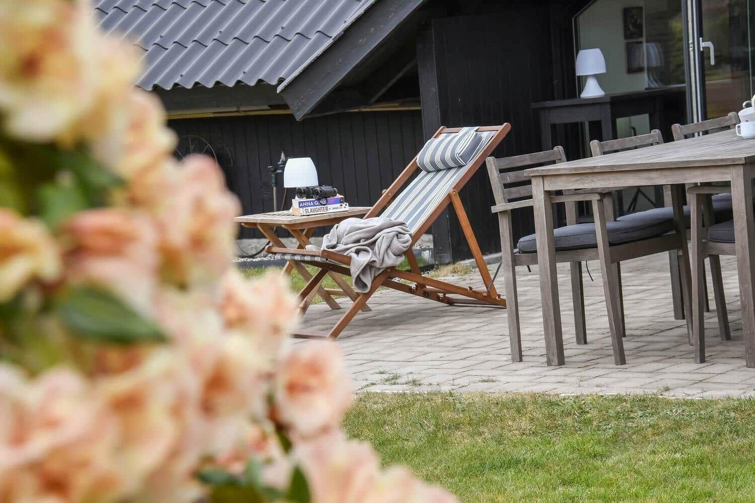 Terrasse mit Liegestuhl, Tisch und Stühlen. Im Vordergrund Blumen.