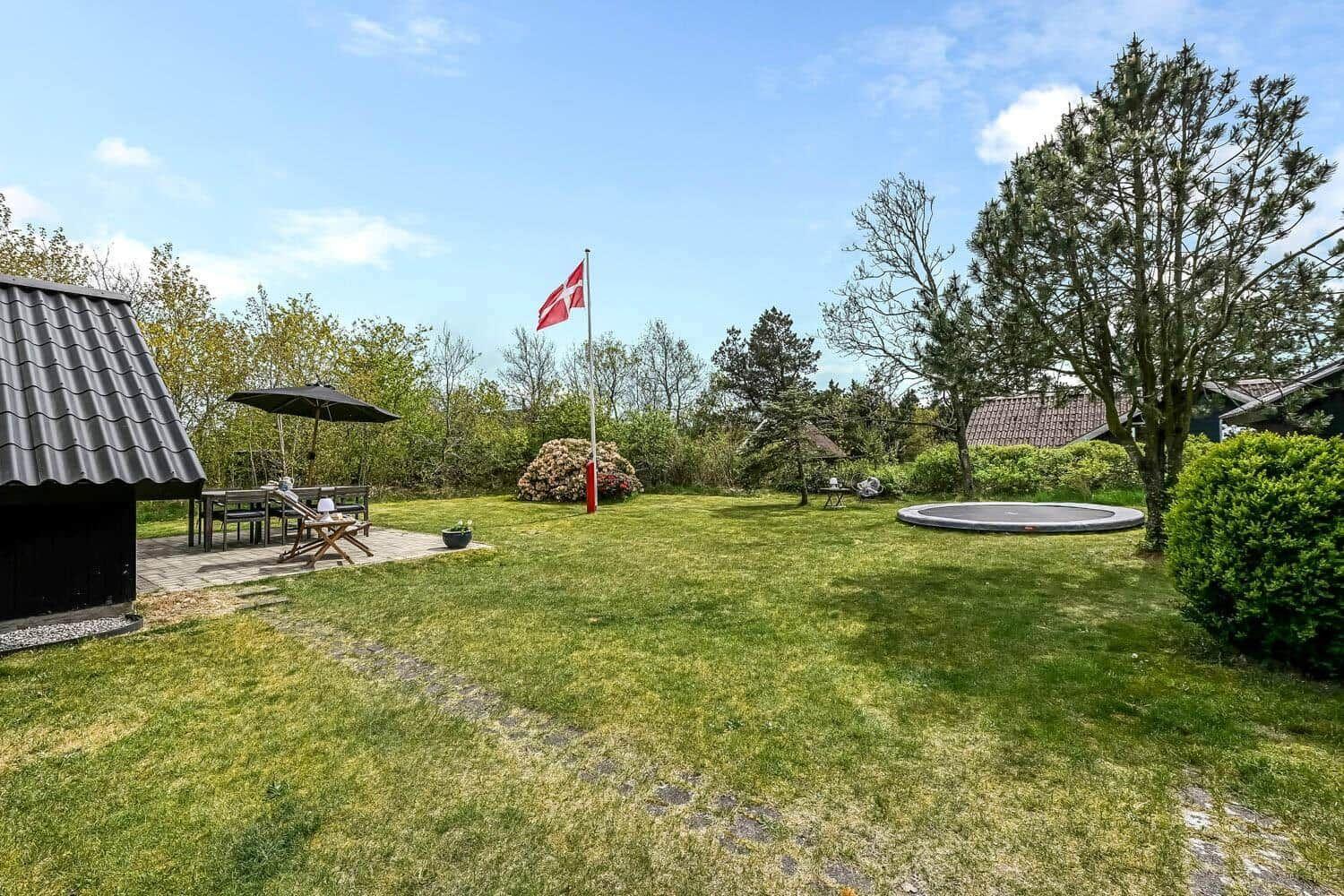 Garten mit Grillplatz, Trampolin und dänischer Flagge. Grasfläche und Bäume umgeben den Außenbereich.