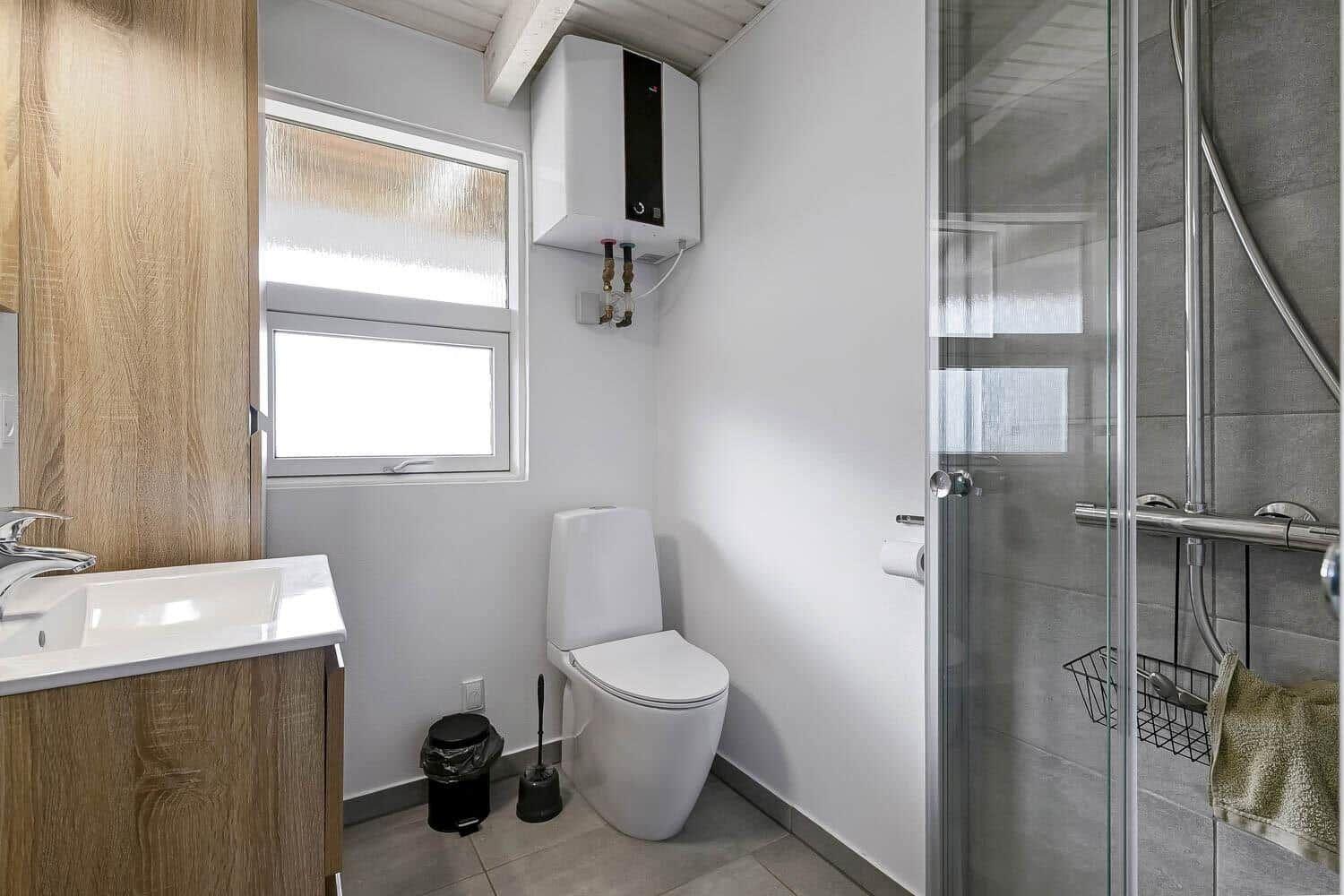 Badezimmer mit Dusche, Toilette und Waschbecken. Fenster und Heizung sichtbar.
