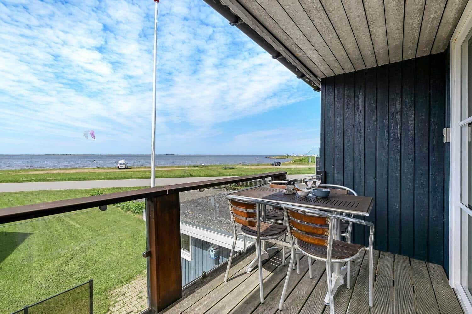 Terrasse mit Tisch und Stühlen, Blick auf Wasser und Strand.
