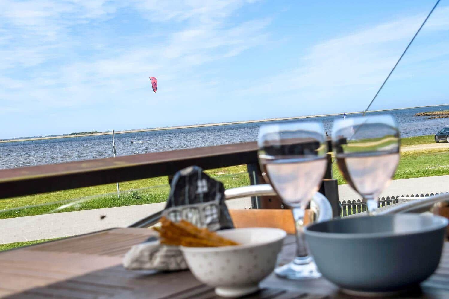 Tisch mit Gläsern und Schalen auf Terrasse mit Blick auf Wasser und Kitesurfer.