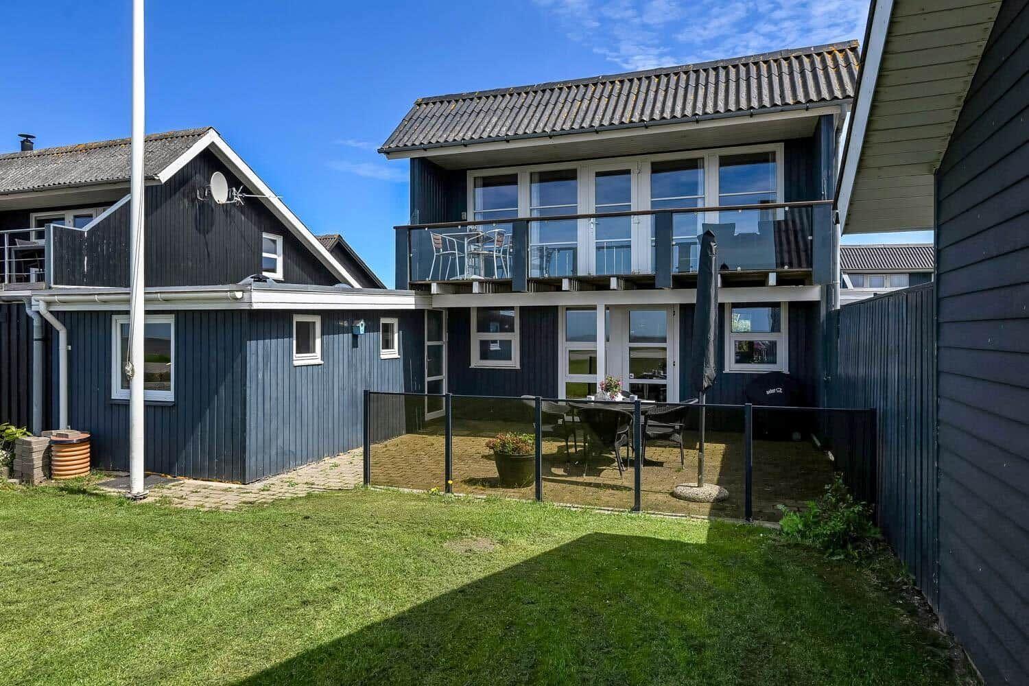 Zweistöckiges Haus mit Balkon, Garten und Terrasse mit Sitzgelegenheiten.