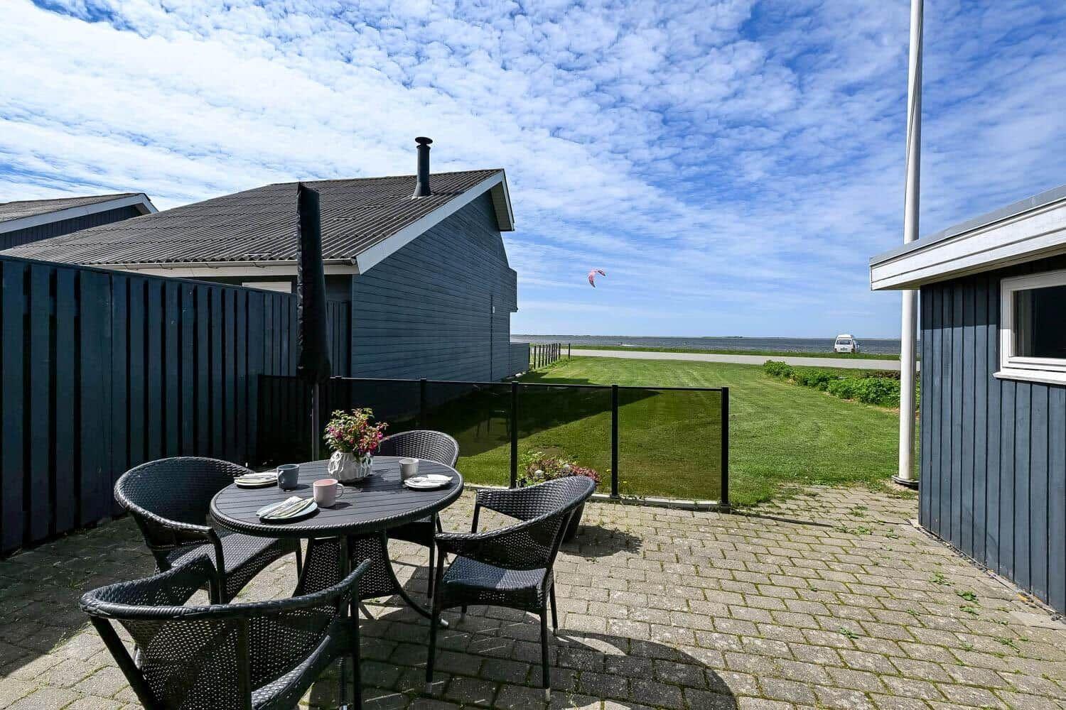 Terrasse mit Tisch und Stühlen, Blick auf Grasfläche und Strand.