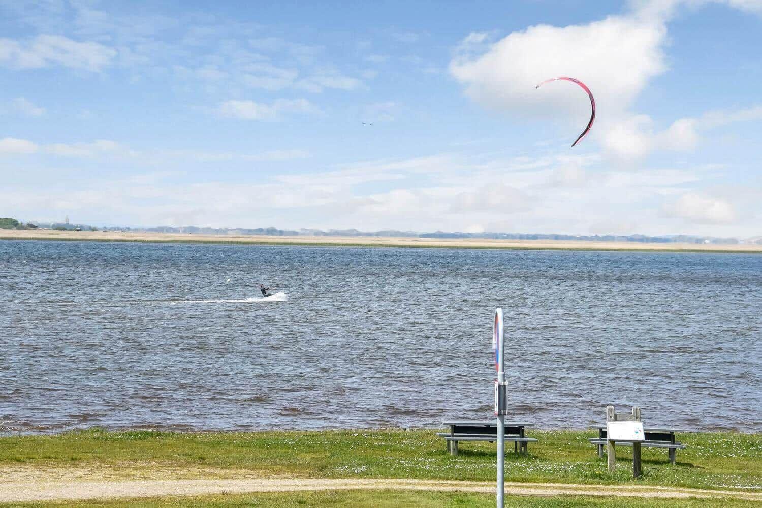 Kitesurfer auf dem Wasser mit rotem Segel im Himmel.