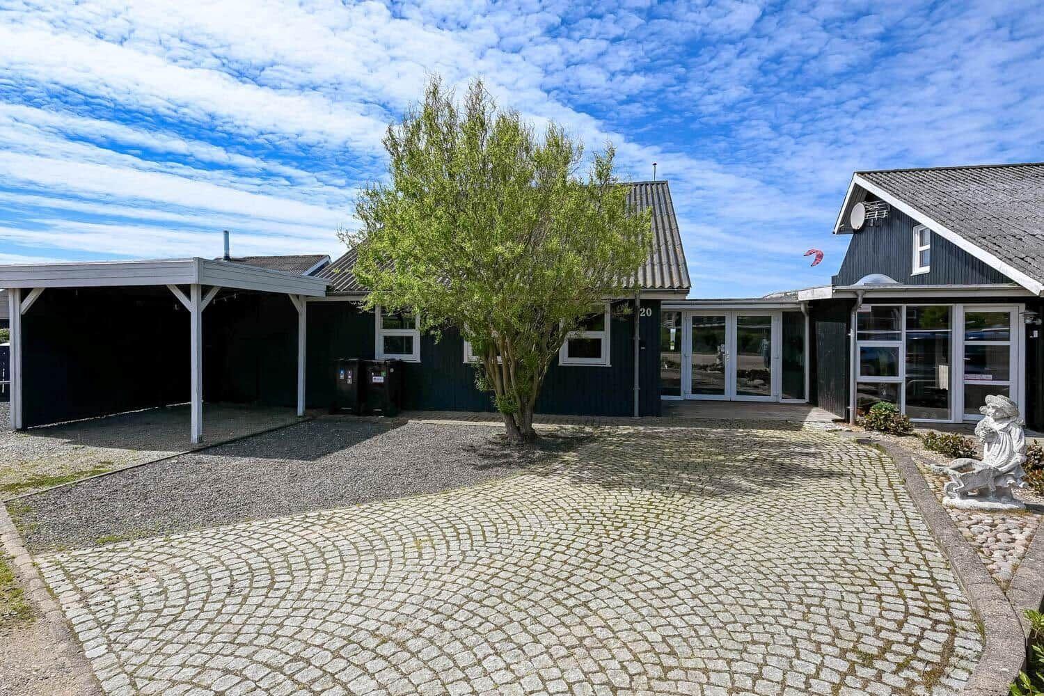 Haus mit Kiesweg, Carport und Baum unter blauem Himmel.