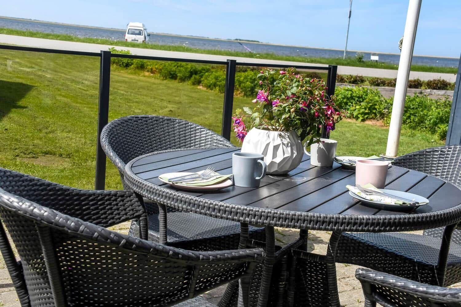 Rundtisch mit Stühlen auf Terrasse. Blumen und Tassen sind darauf platziert.