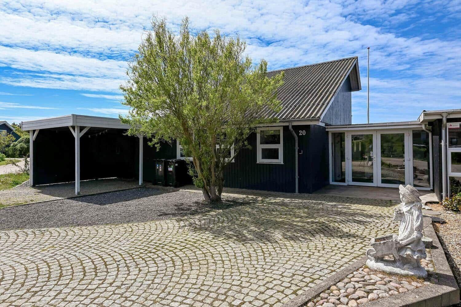 Ein dunkelblauer Ferienhaus mit Garage und Steinweg unter blauem Himmel.