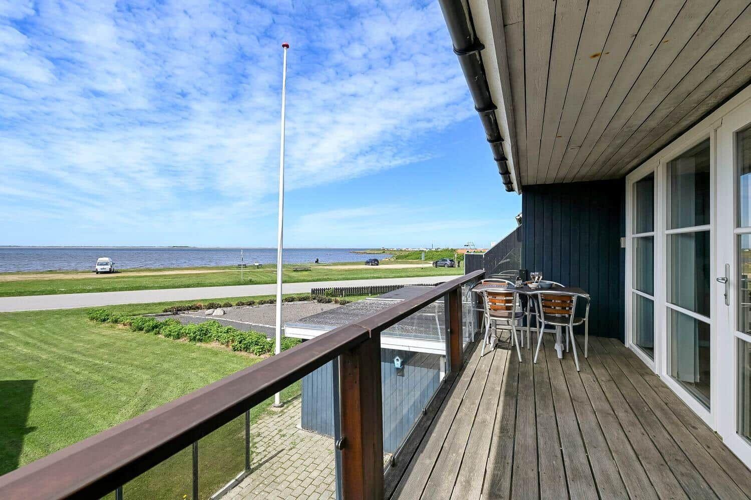 Terrasse mit Tisch und Stühlen, Blick auf Grünfläche und Wasser.
