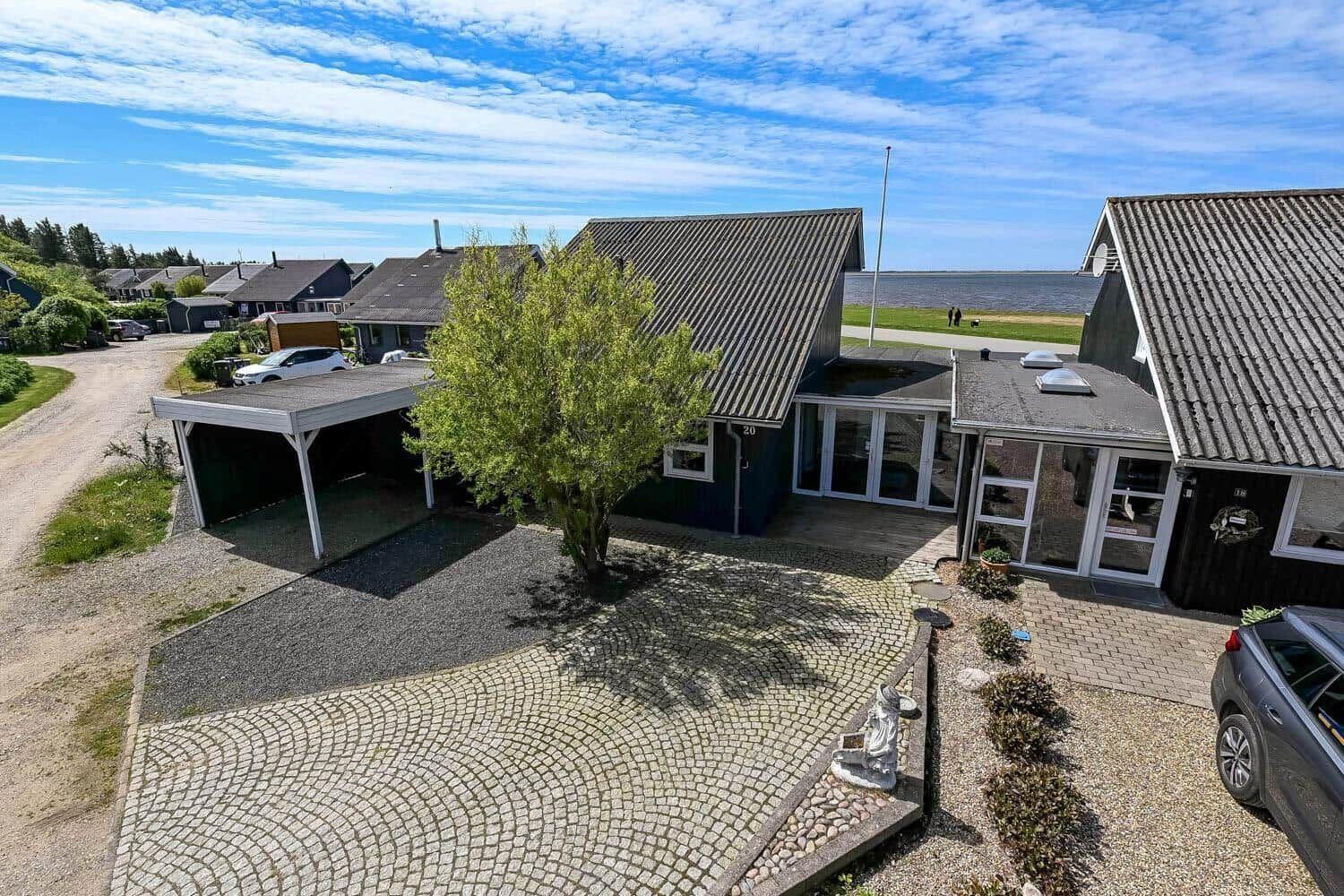 Haus mit Terrasse, Garage und gepflastertem Hof. Blick auf Wasser und Grünflächen.