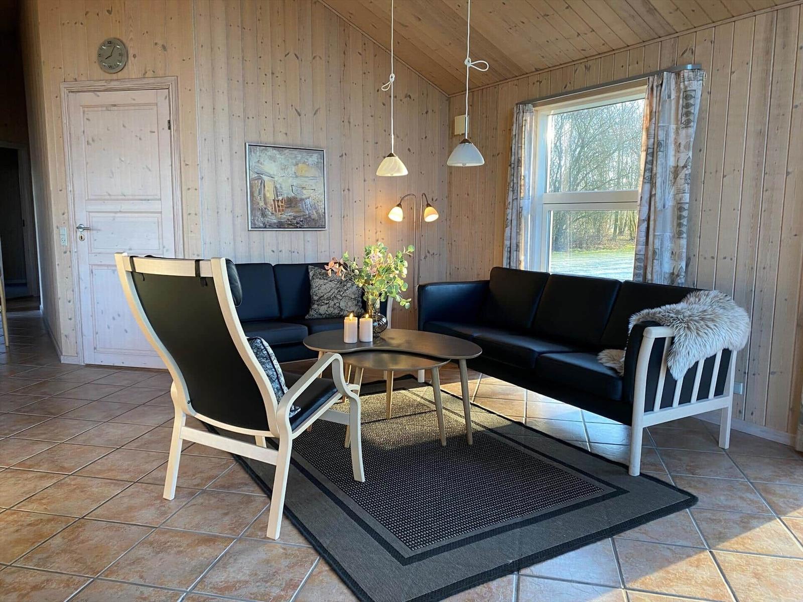 Wohnzimmer mit Holzwand, zwei schwarzen Sofas, einem Stuhl und einem Tisch.