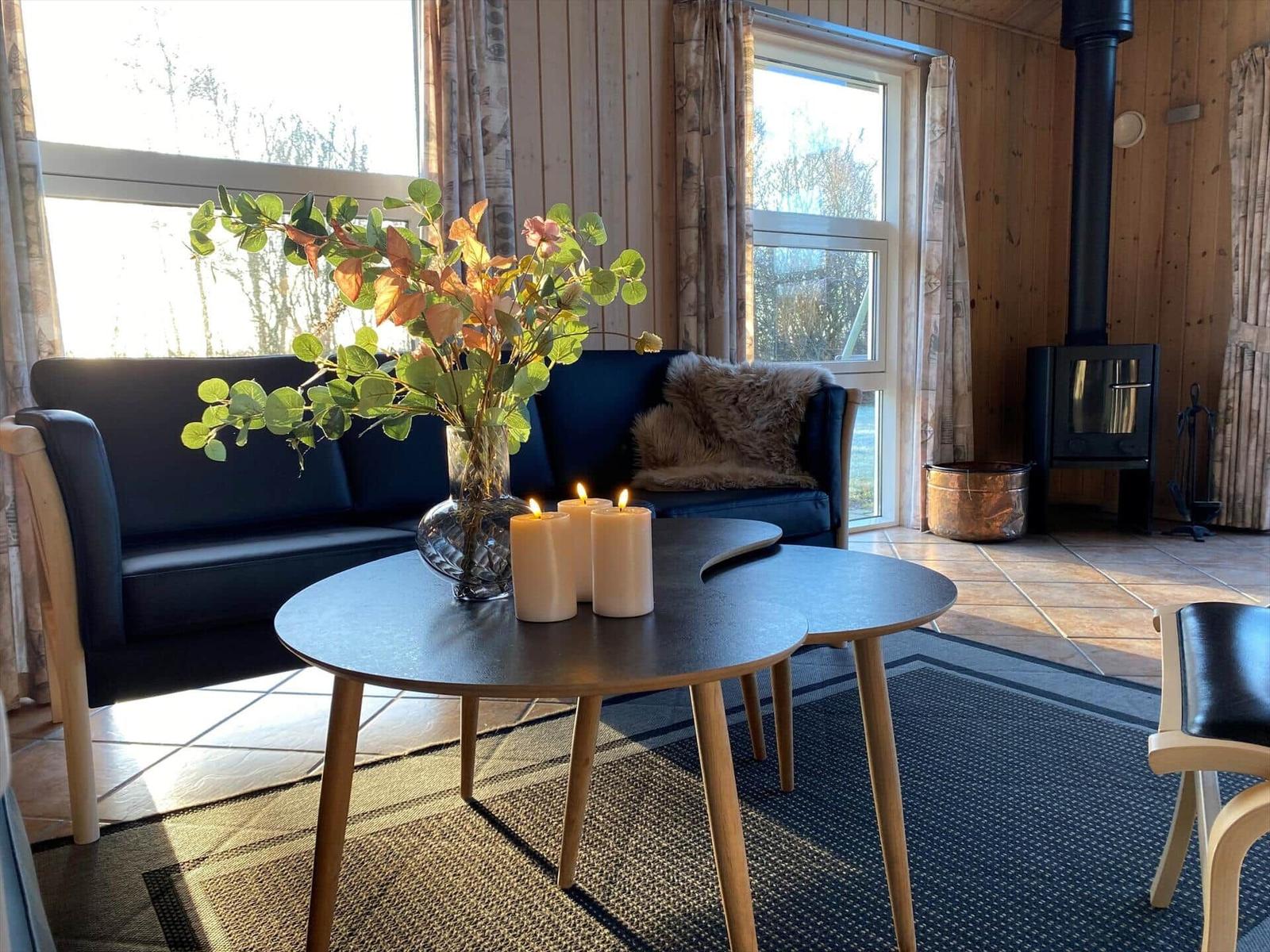 Ein Wohnzimmer mit Sofa, Tisch, Kerzen und Pflanze. Holzwände und Fenster.