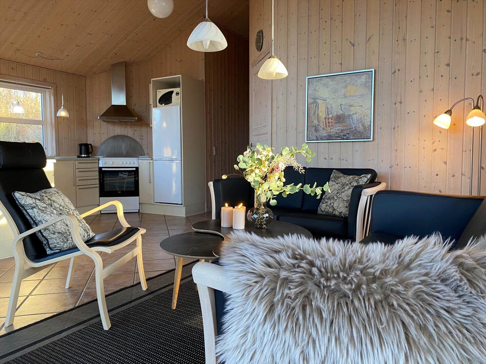 Wohnbereich mit Sofa, Stuhl und Küchenzeile. Holzwände und Beleuchtung.