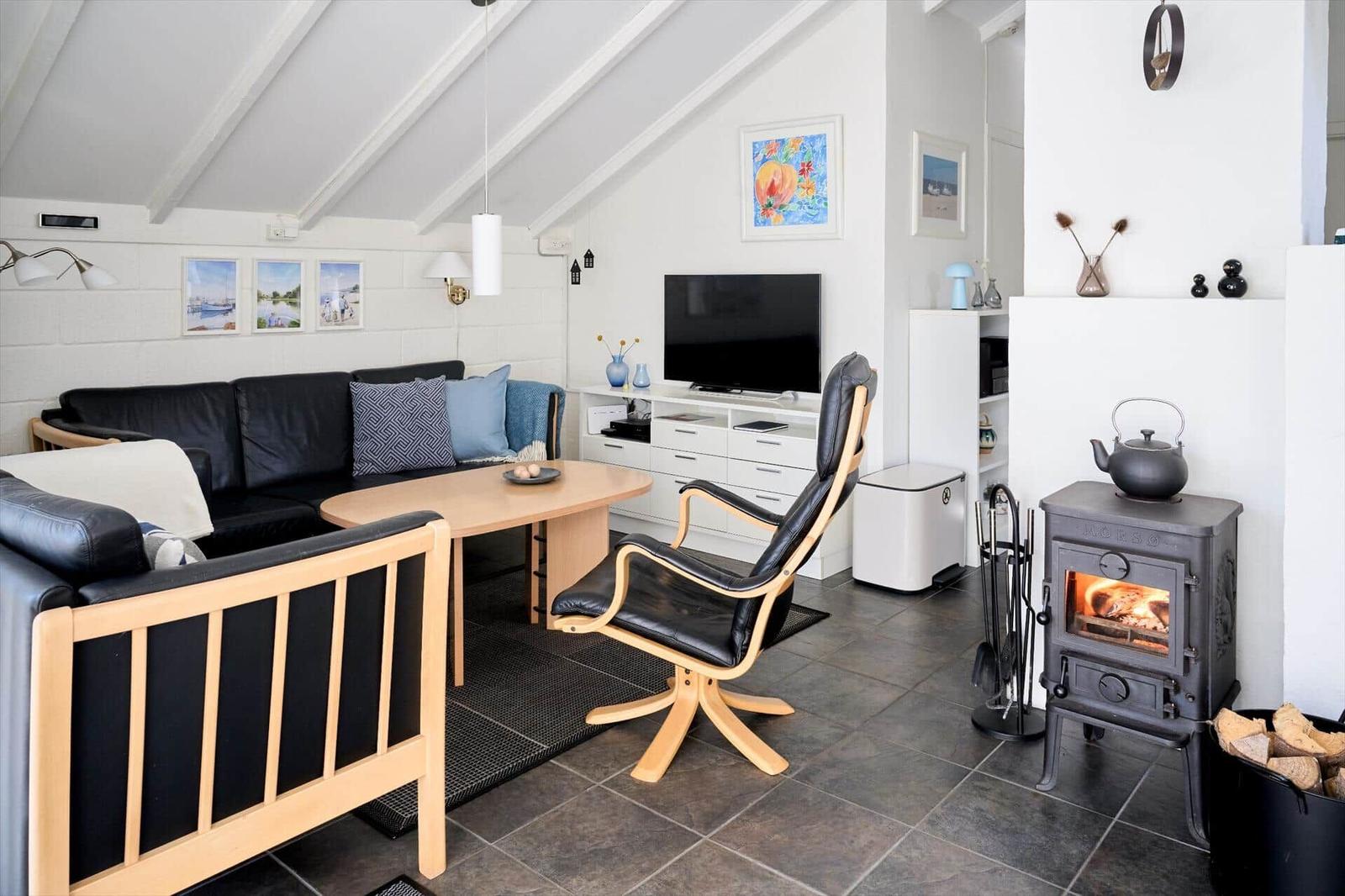 Wohnzimmer mit Sofa, Stuhl, Fernseher und Kaminofen.