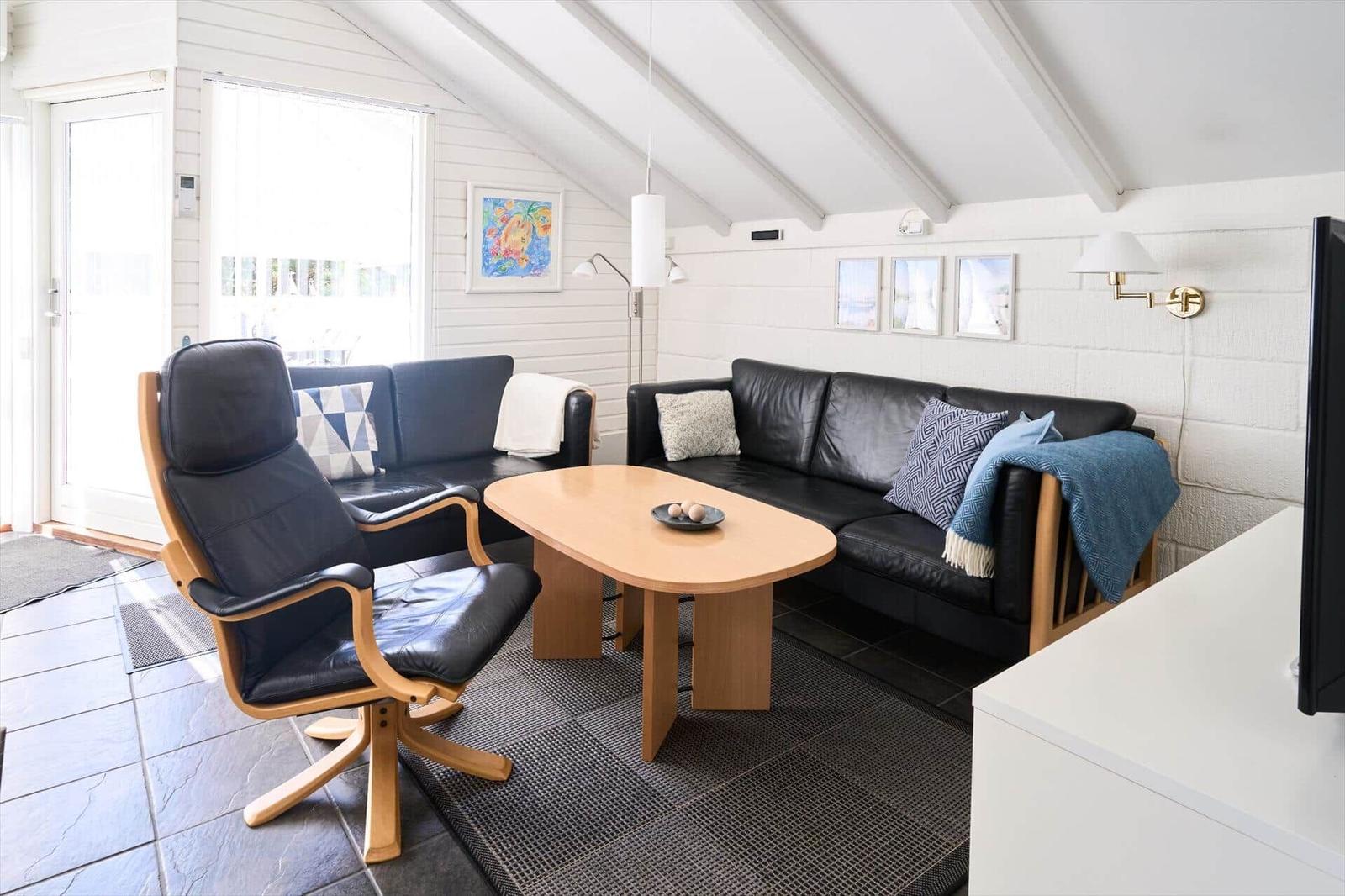 Wohnzimmer mit schwarzen Ledermöbeln, Holztisch und schrägen weißen Wänden.