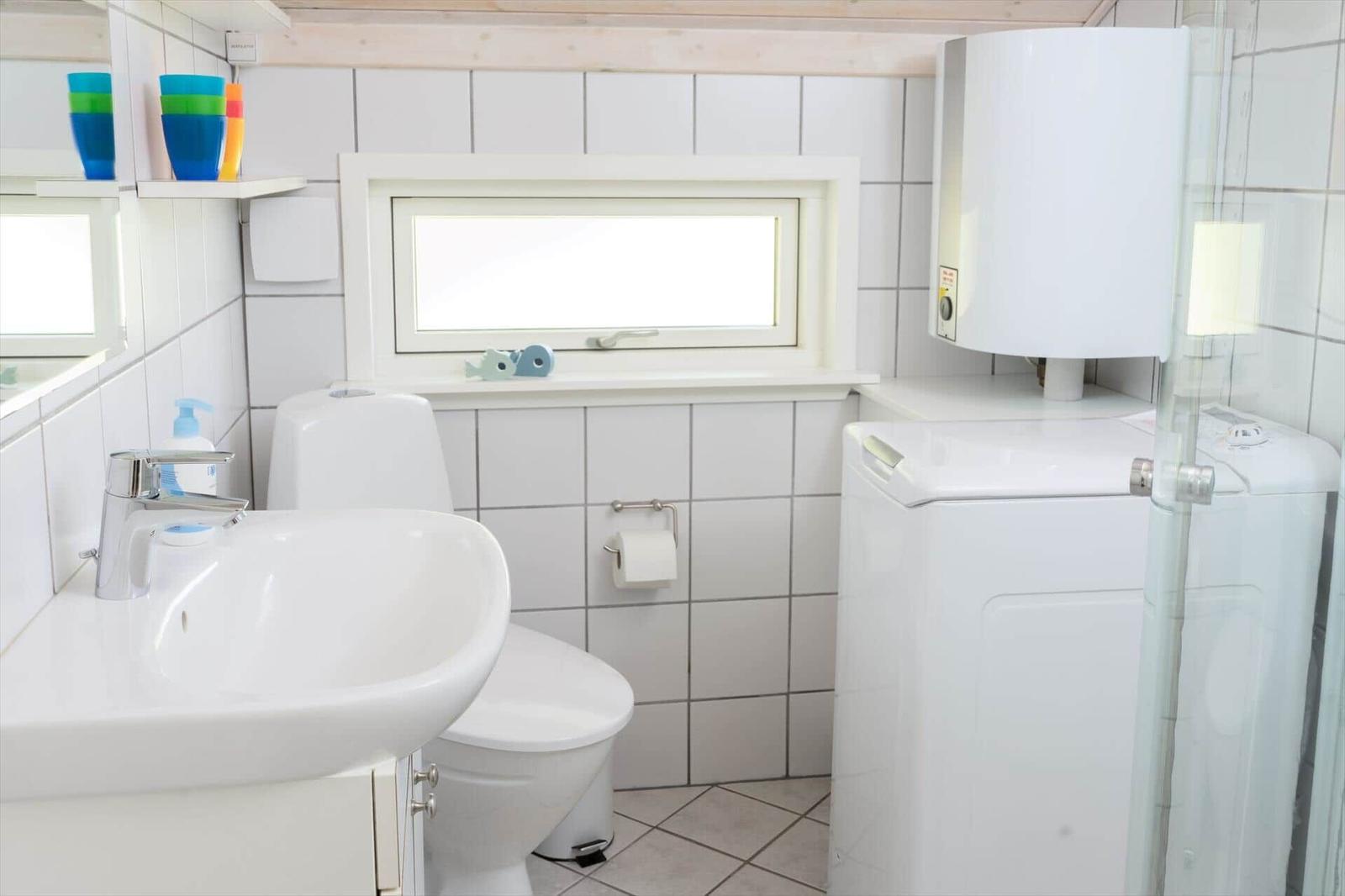 Badezimmer mit Waschmaschine, Toilette und Waschbecken. Fenster und farbige Tassen sichtbar.