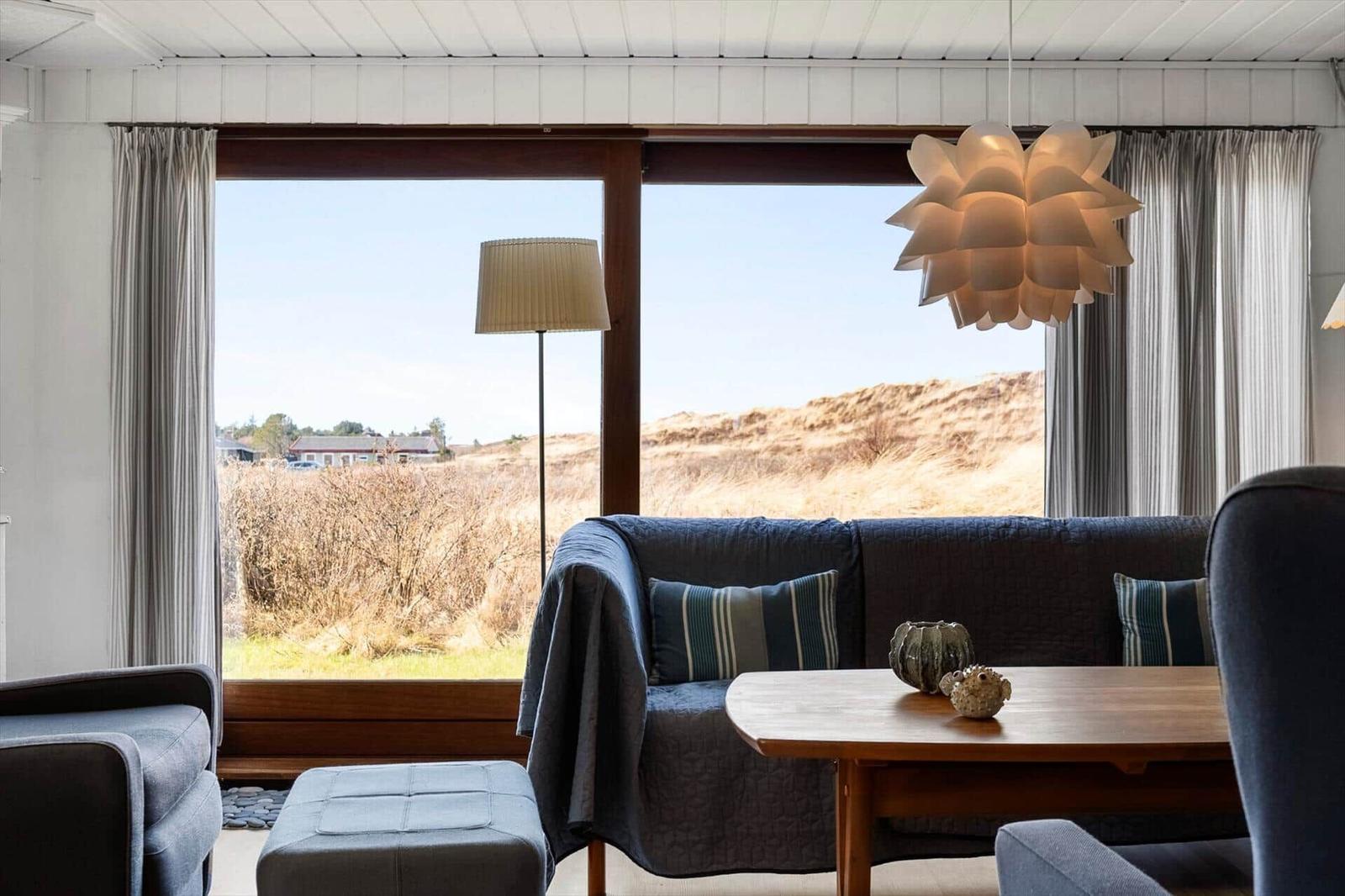 Wohnzimmer mit Sofa, Tisch und Blick auf Dünen