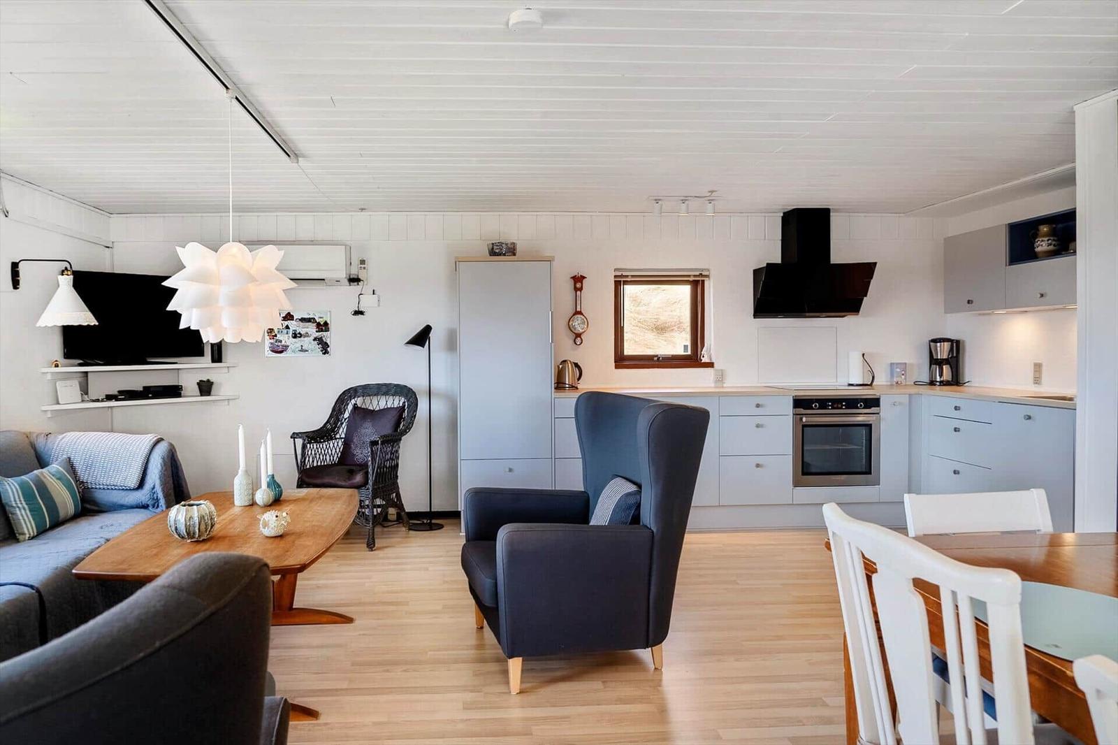 Wohnküche mit Sofa, Sessel, Esstisch und Küchenschränken.