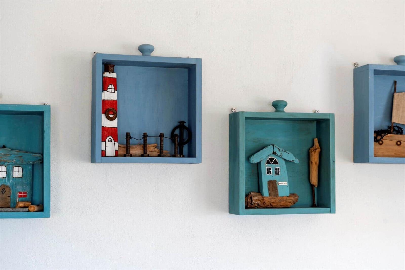 Wand mit blauen Holzkästen, die maritime Dekorationen enthalten.