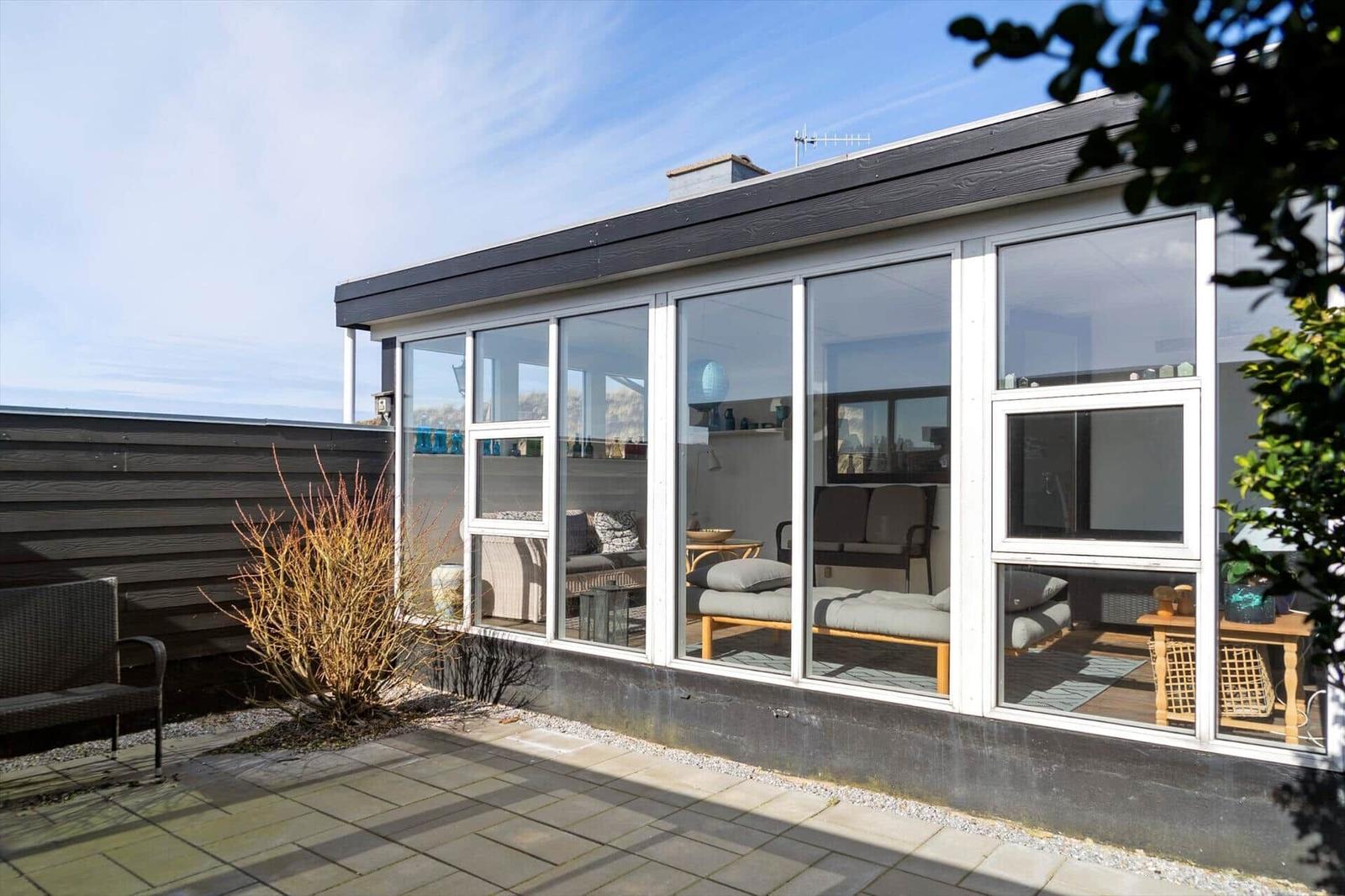Modernes Haus mit großem Glasbereich und Terrasse. Sicht auf Wohnbereich mit Sofa und Tisch.