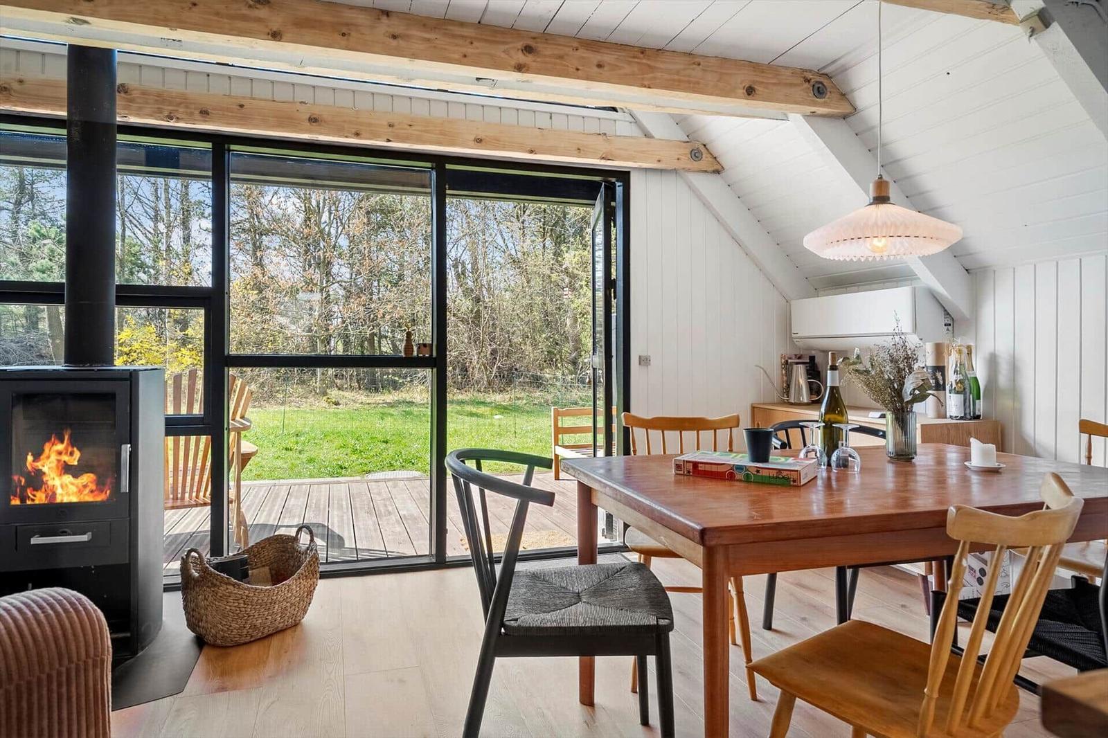 Essbereich mit Holztisch, Stühlen und Kamin. Große Fensterfront mit Blick auf Garten.
