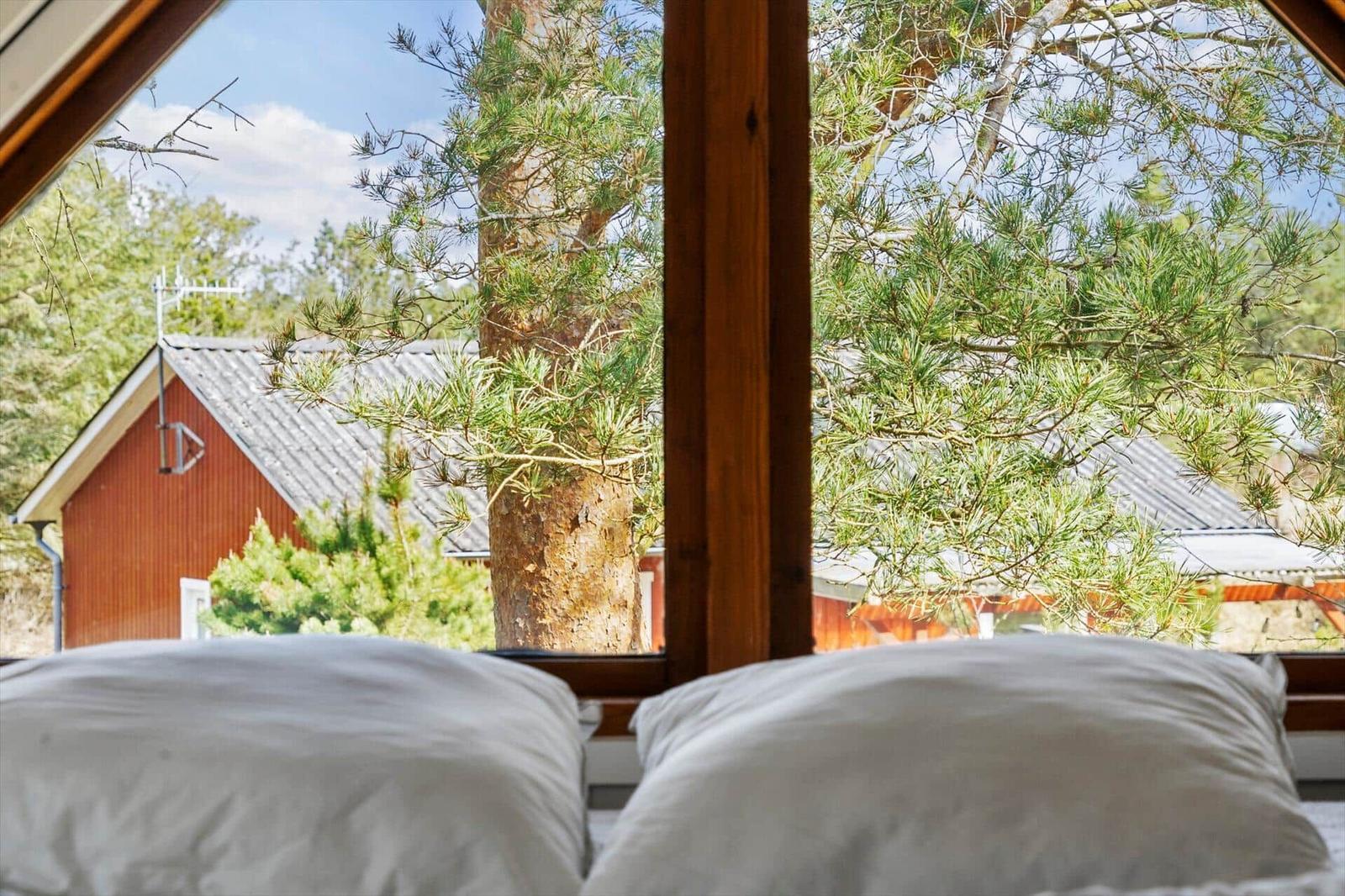 Zwei Kissen vor einem Fenster mit Blick auf einen Baum und ein rotes Gebäude.