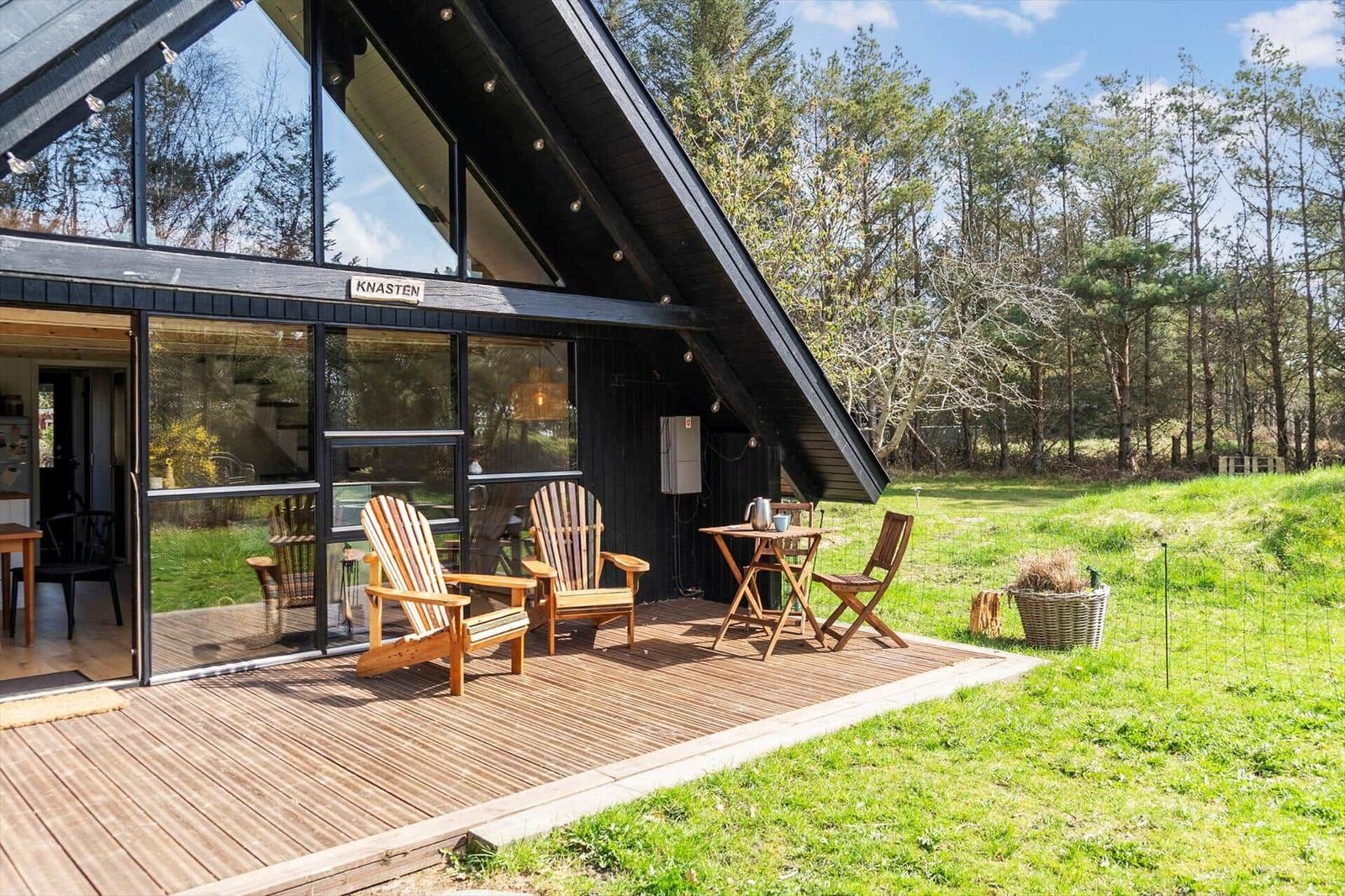 Holzterrasse mit Sitzgelegenheiten vor einem modernen Haus mit großem Glasbereich.