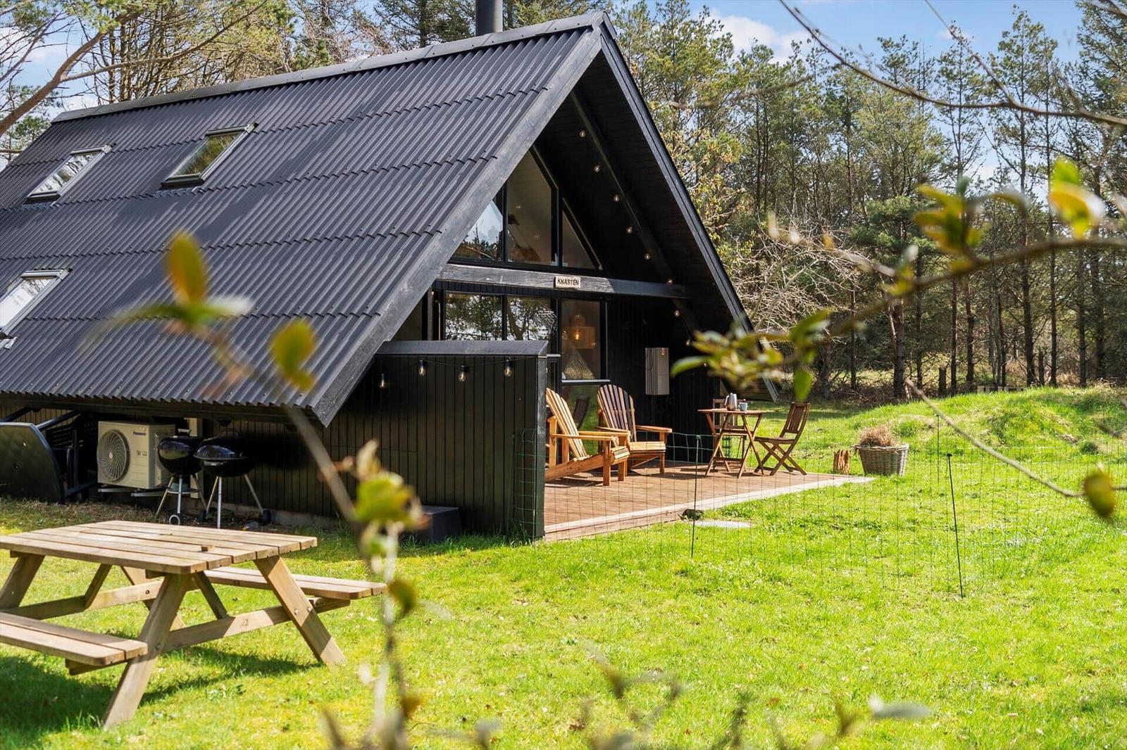 Hütte mit Terrasse, Grill und Picknicktisch im Grünen.