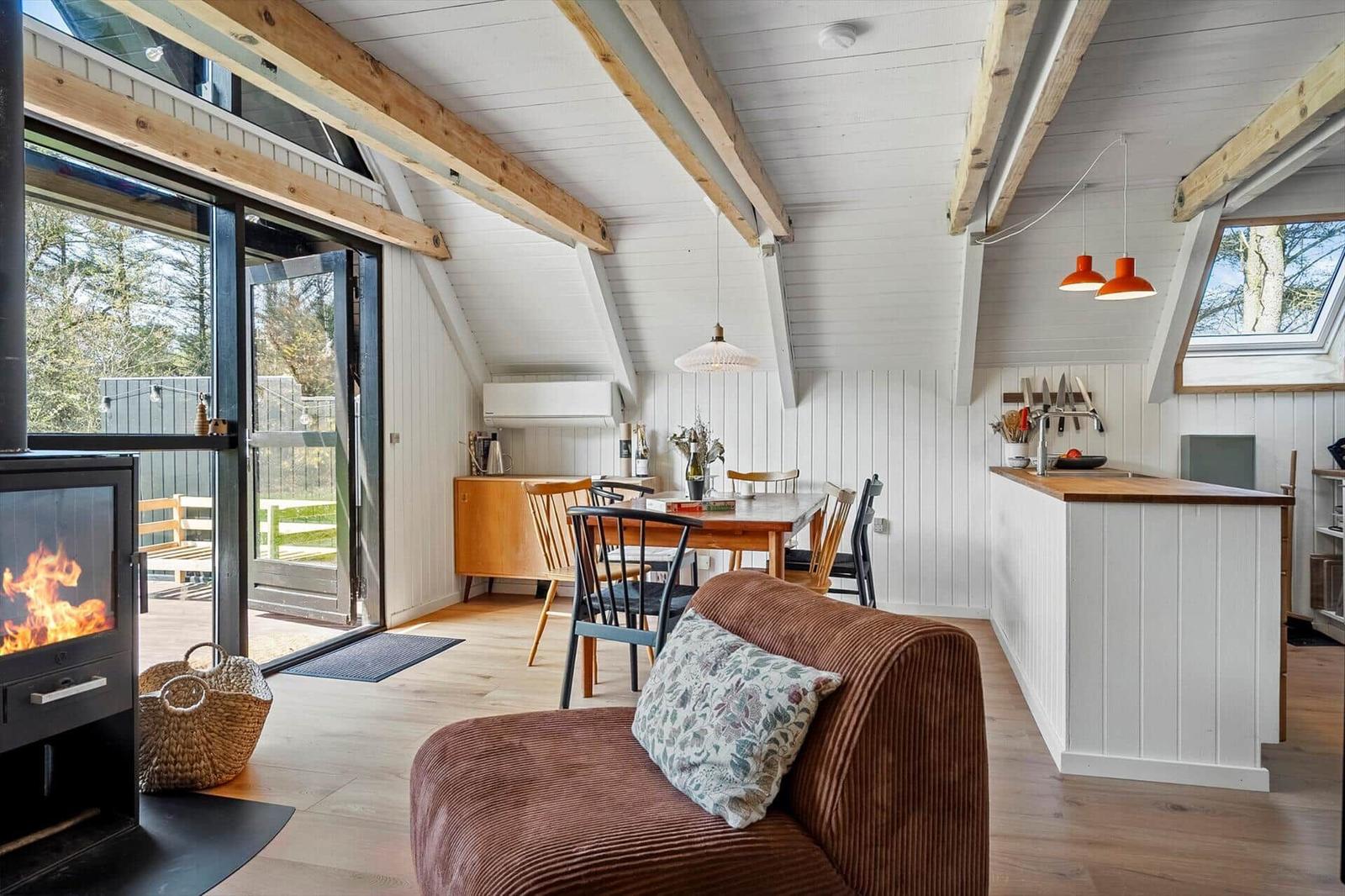 Wohnbereich mit Kamin, Essbereich und Kücheninsel unter Holzbalkendecke.