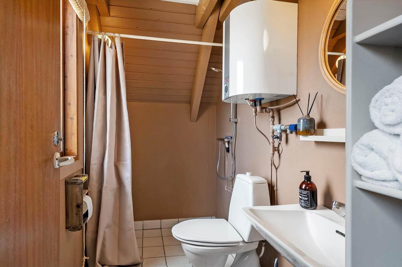 Badezimmer mit Dusche, Toilette und Waschbecken. Holzdecke und -wände.