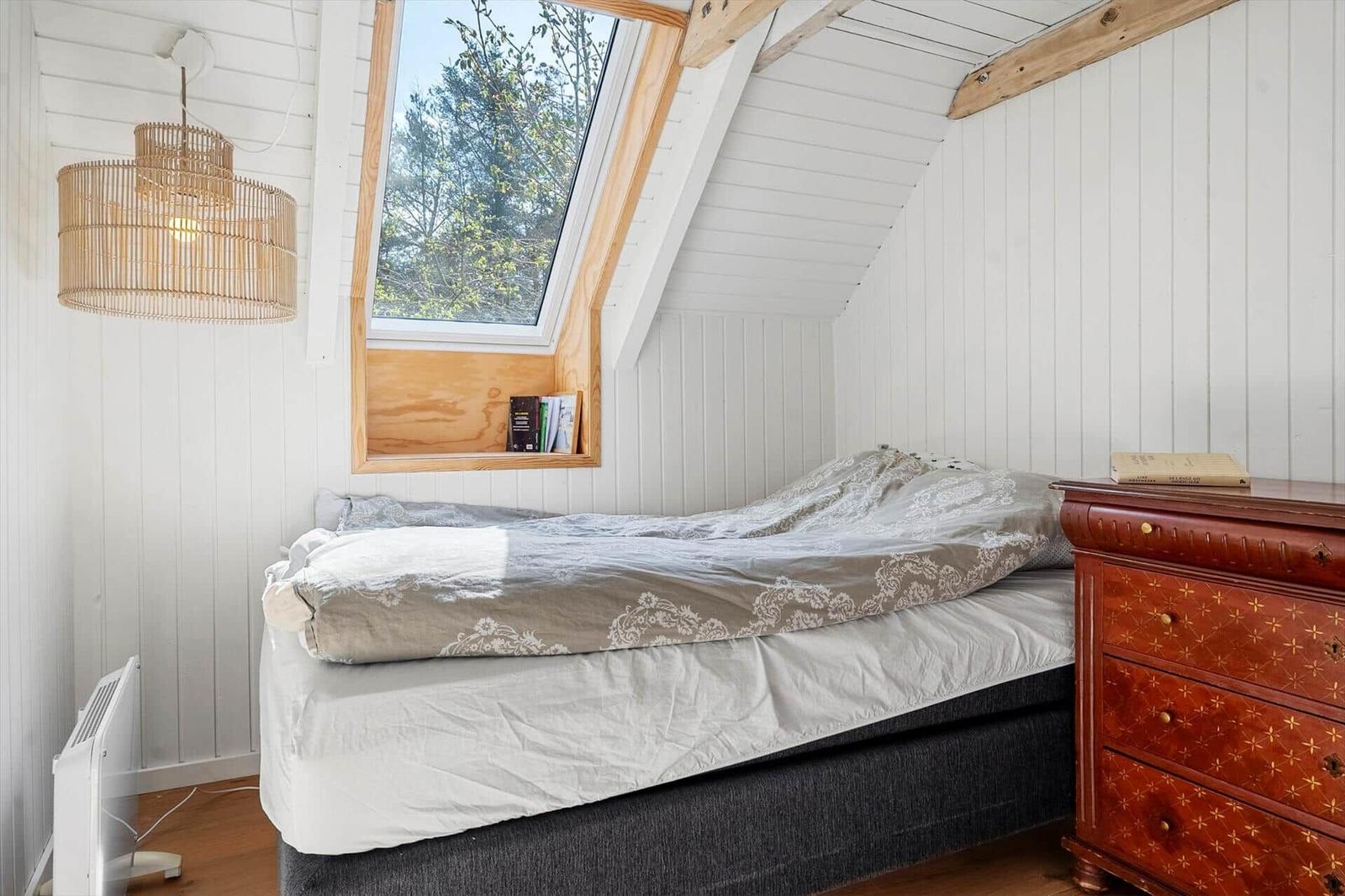 Schlafzimmer mit Dachfenster, Bett und Holzmöbeln.