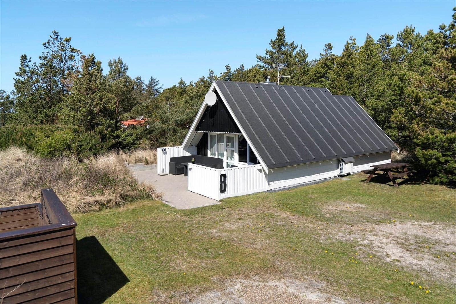Hütte mit Terrasse, Garten und Picknicktisch. Umgeben von Bäumen und Gras.
