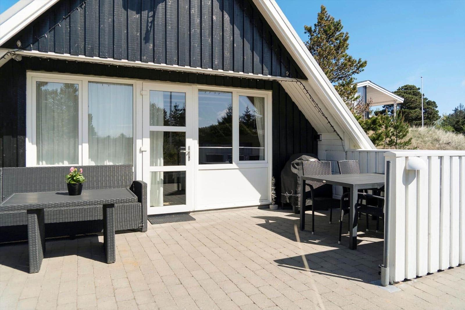 Terrasse mit Tisch, Stühlen und Sitzbank vor einem Haus mit weißen Fenstern.