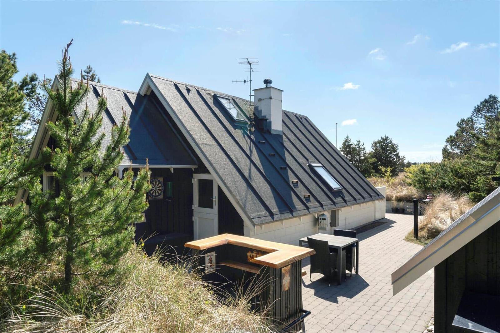 Ein Haus mit schwarzem Dach und weißer Fassade, umgeben von Bäumen und einem gepflasterten Hof.