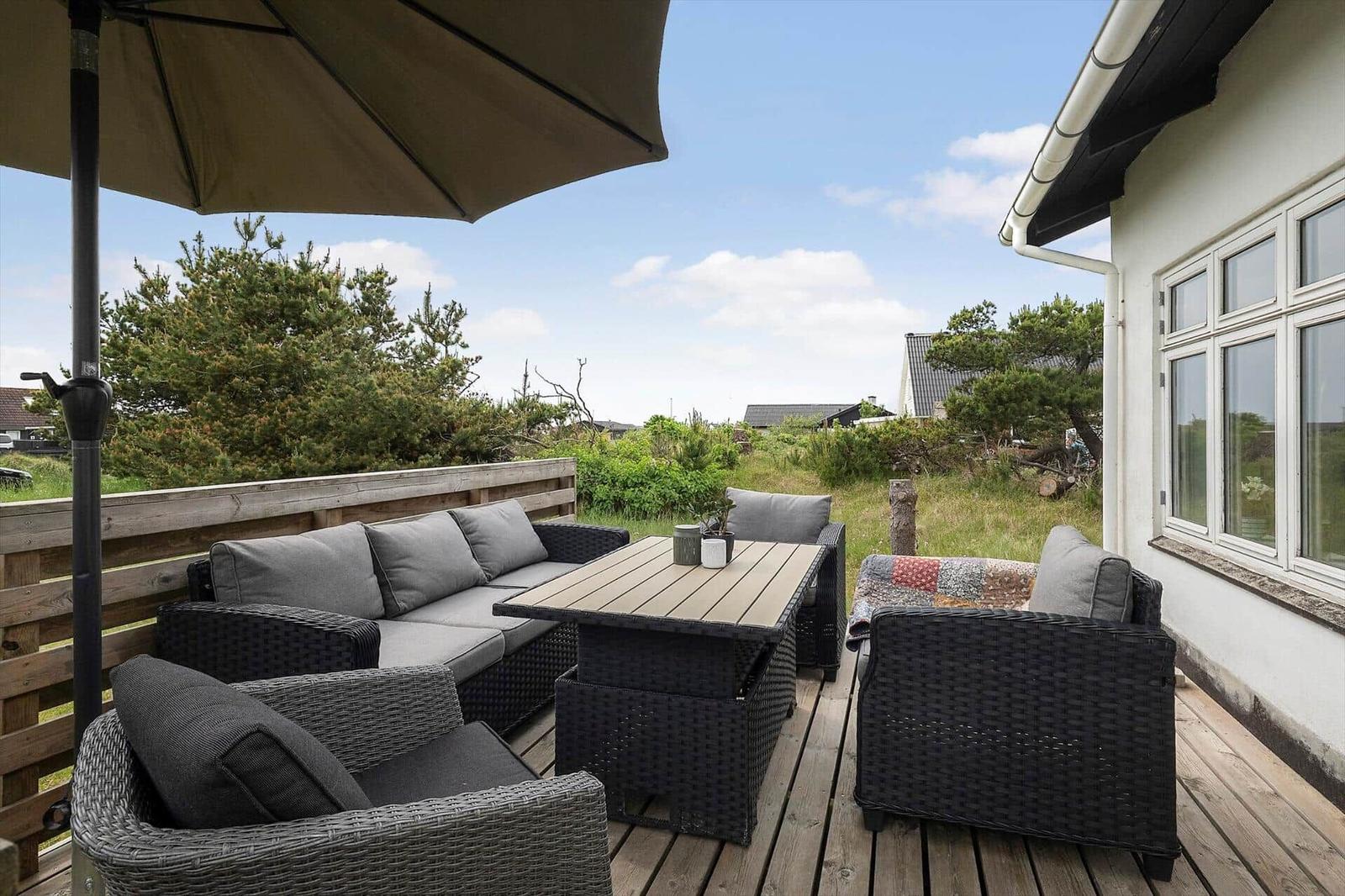 Terrasse mit Sitzgruppe, Tisch und Sonnenschirm. Blick auf Grünflächen und Hauswand.